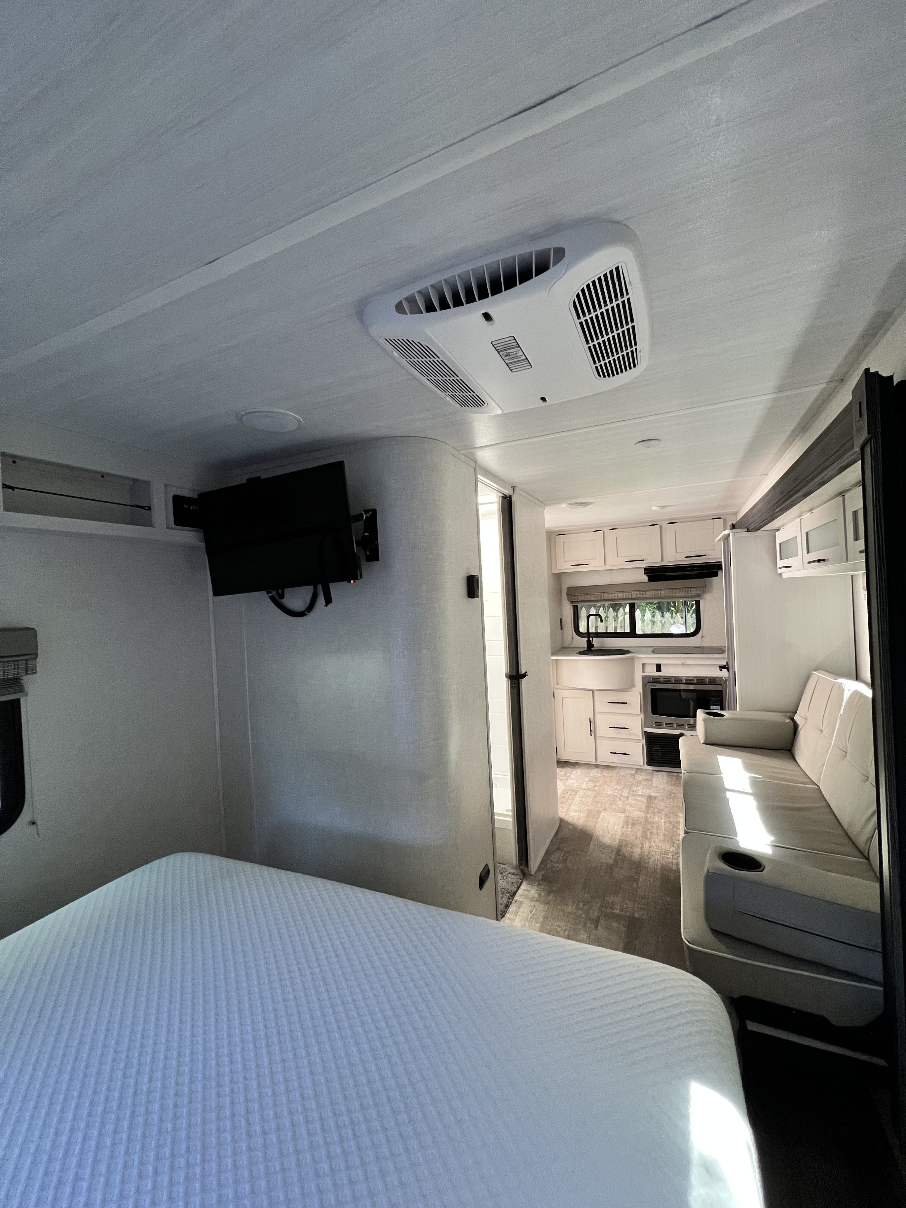 View inside a modern RV rental: bedroom with bed & TV in foreground, leading to kitchen & living area with sofa.. R-Pod R-Pod Trailer 2022