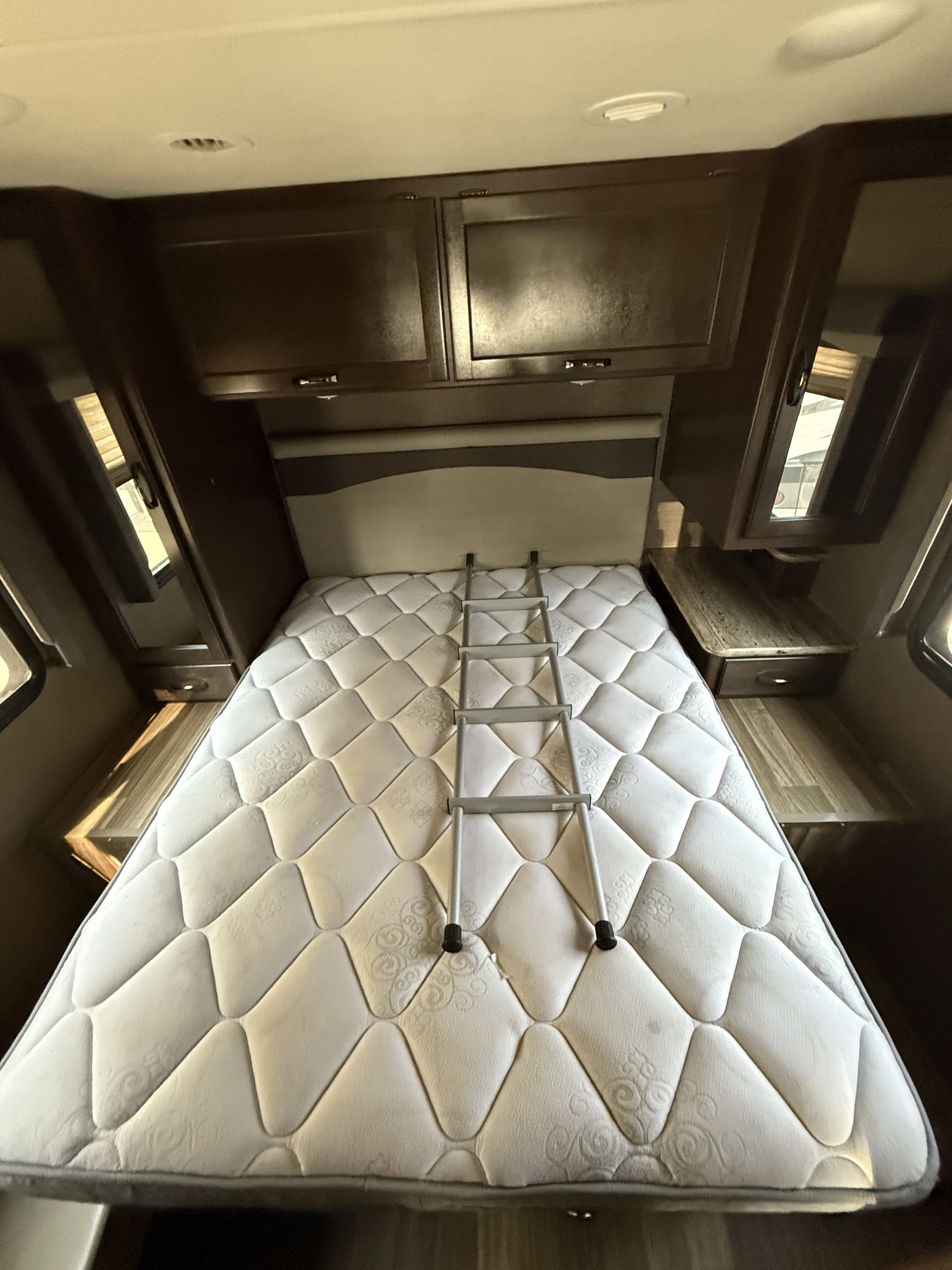 RV rental bedroom: a cozy space with a quilted mattress, a ladder, dark cabinets, and bedside tables.. Thor Motor Coach A.C.E 2020