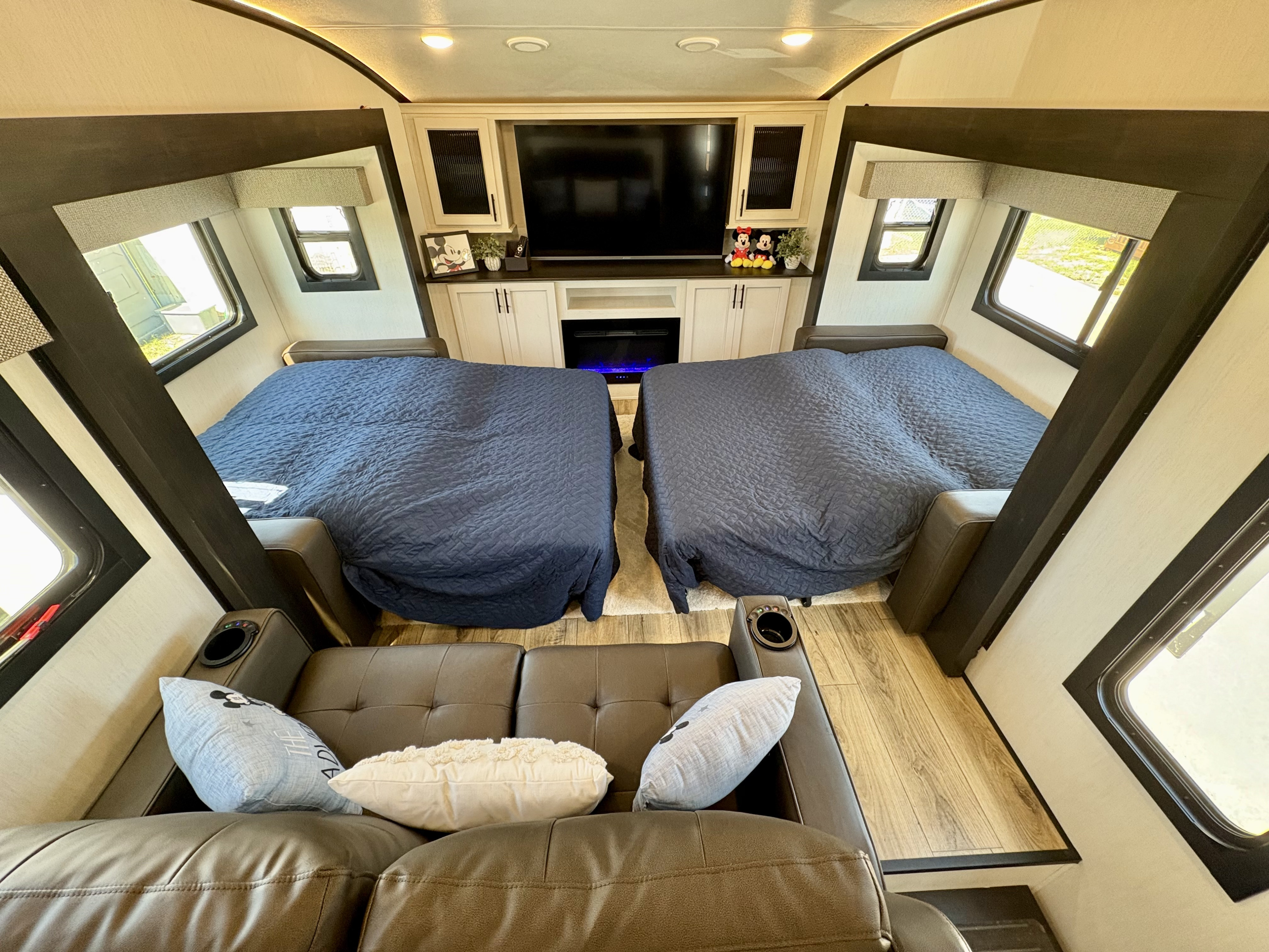 RV rental interior showing two beds, a brown leather sofa with pillows, and a central entertainment unit with TV/fireplace.. Forest River Sabre 2025