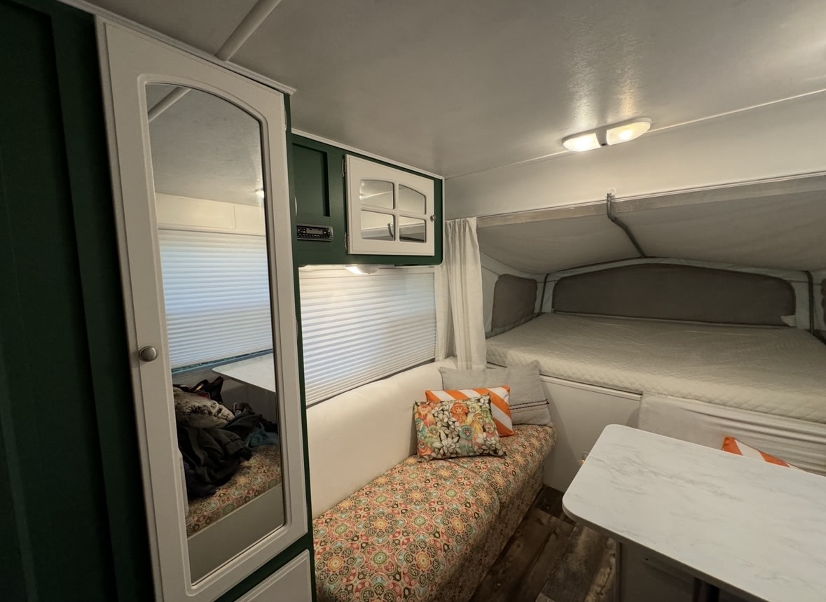 Cozy RV rental interior with bed, colorful bench, mirror cabinet, and storage. Compact and functional travel space.. Starcraft Antiqua 195 CK 2005