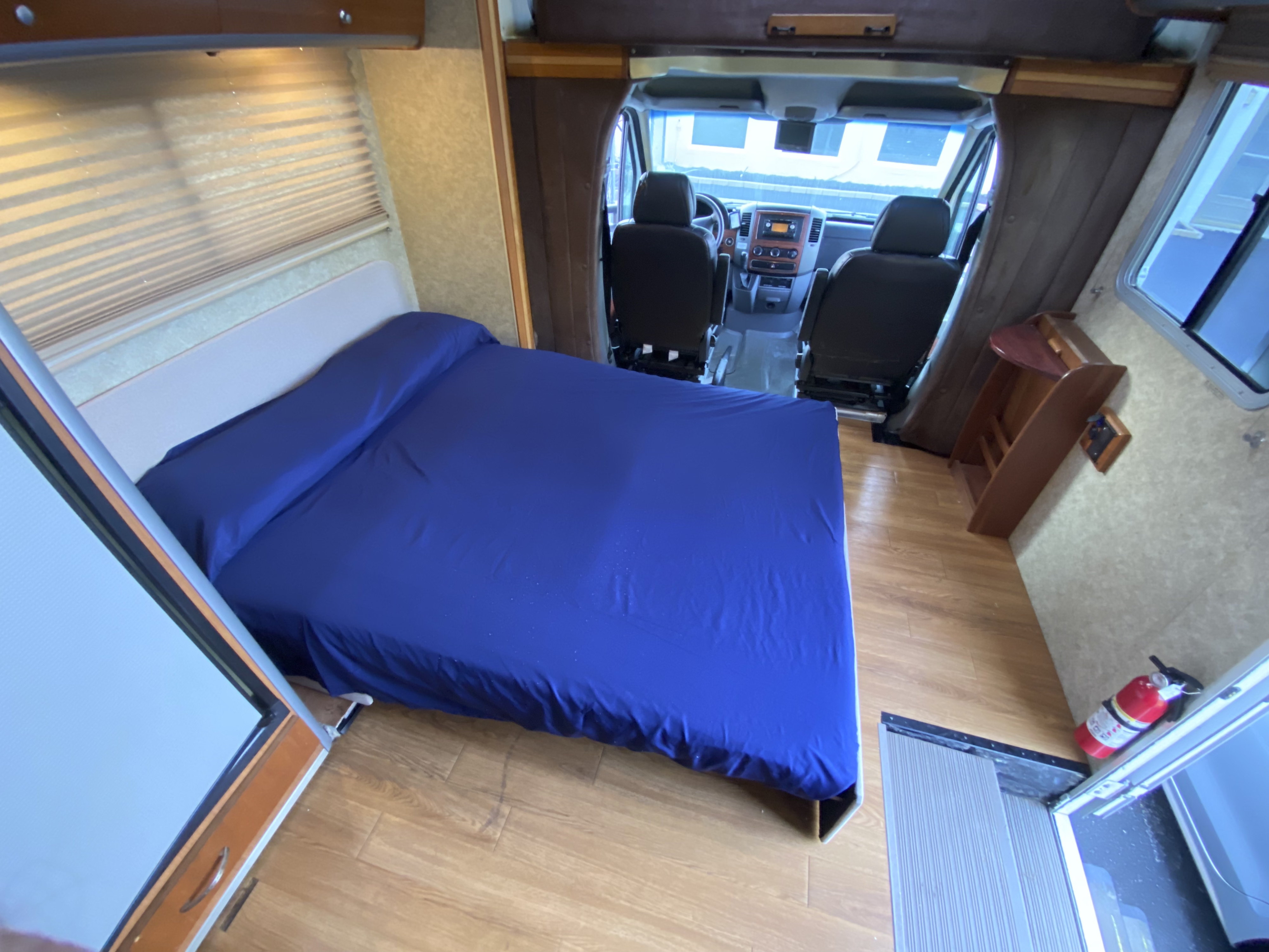 Inside this RV rental, a comfy blue bed is on the left, leading to the front cockpit with driver/passenger seats. Wood flooring throughout.. Winnebago View 2009