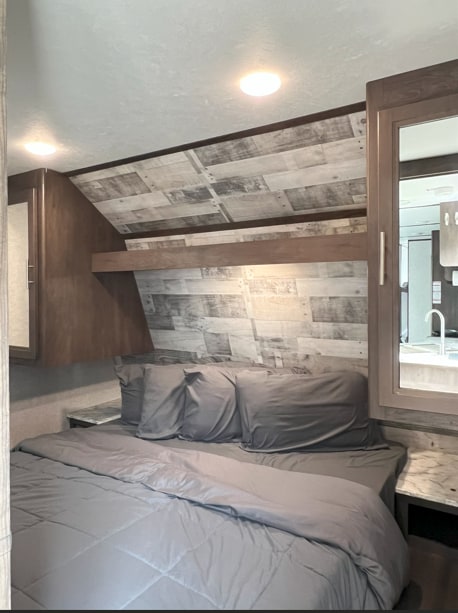 Cozy RV rental bedroom with gray bedding, wood-paneled headboard, and built-in storage for travel.. Dutchmen Coleman Lantern LT 2020