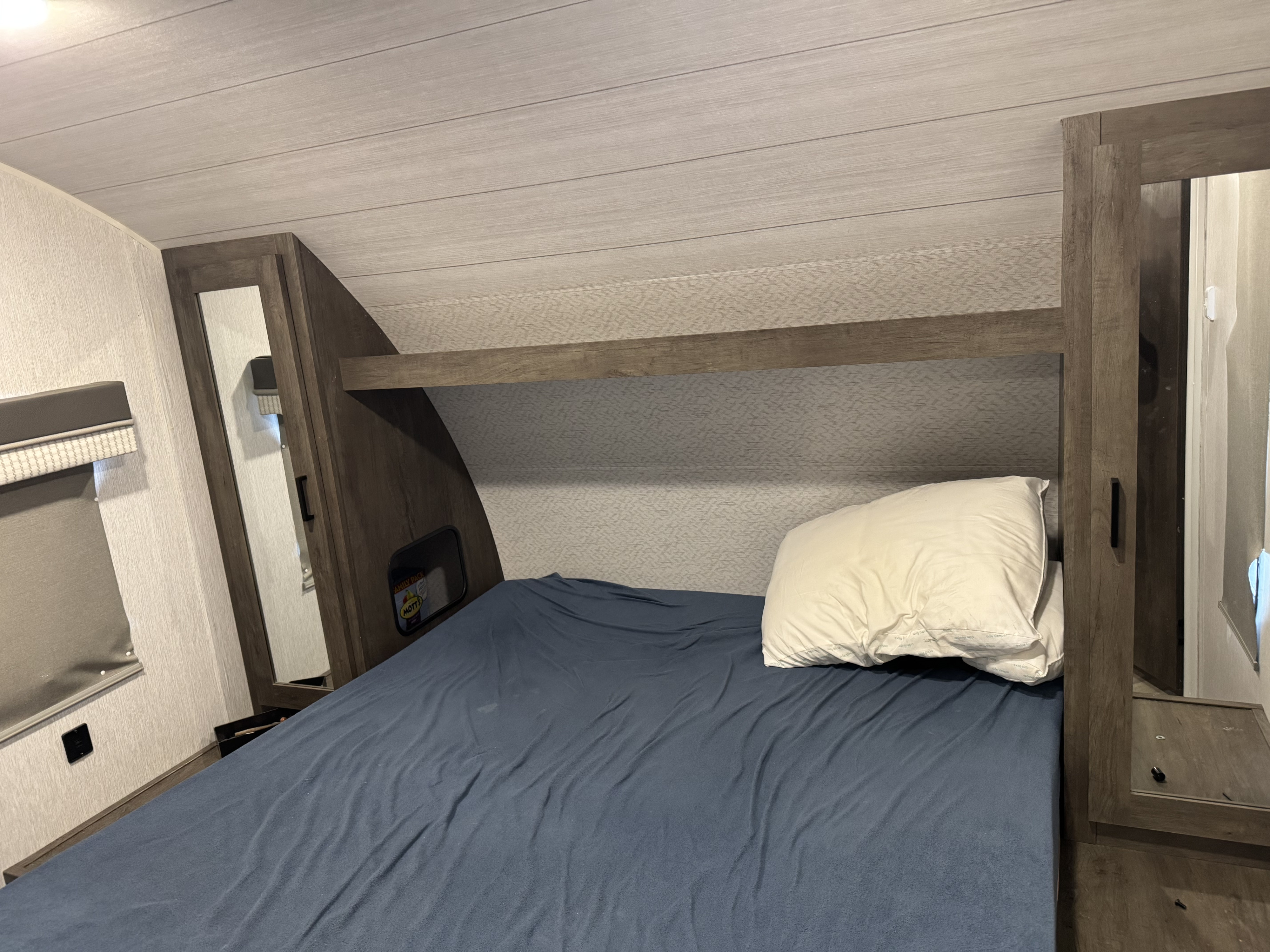 Cozy RV rental bedroom with a blue bed, white pillow, built-in storage, and mirror, showing compact living space.. Forest River Salem Cruise Lite 2022