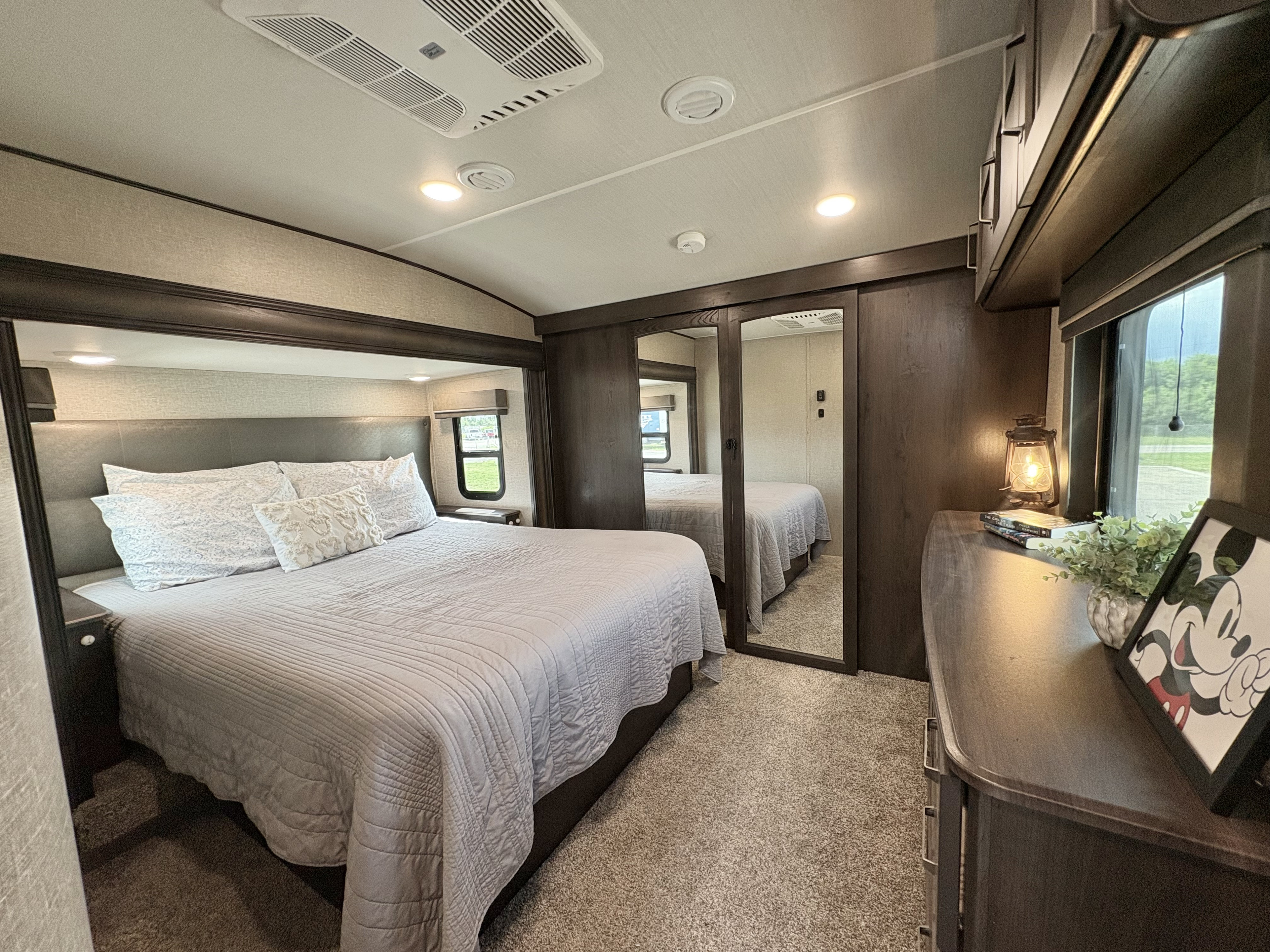 Relax in the plush bedroom of this RV rental, featuring a large bed, mirrored closet, and ceiling AC unit.. Grand Design Reflection 2022