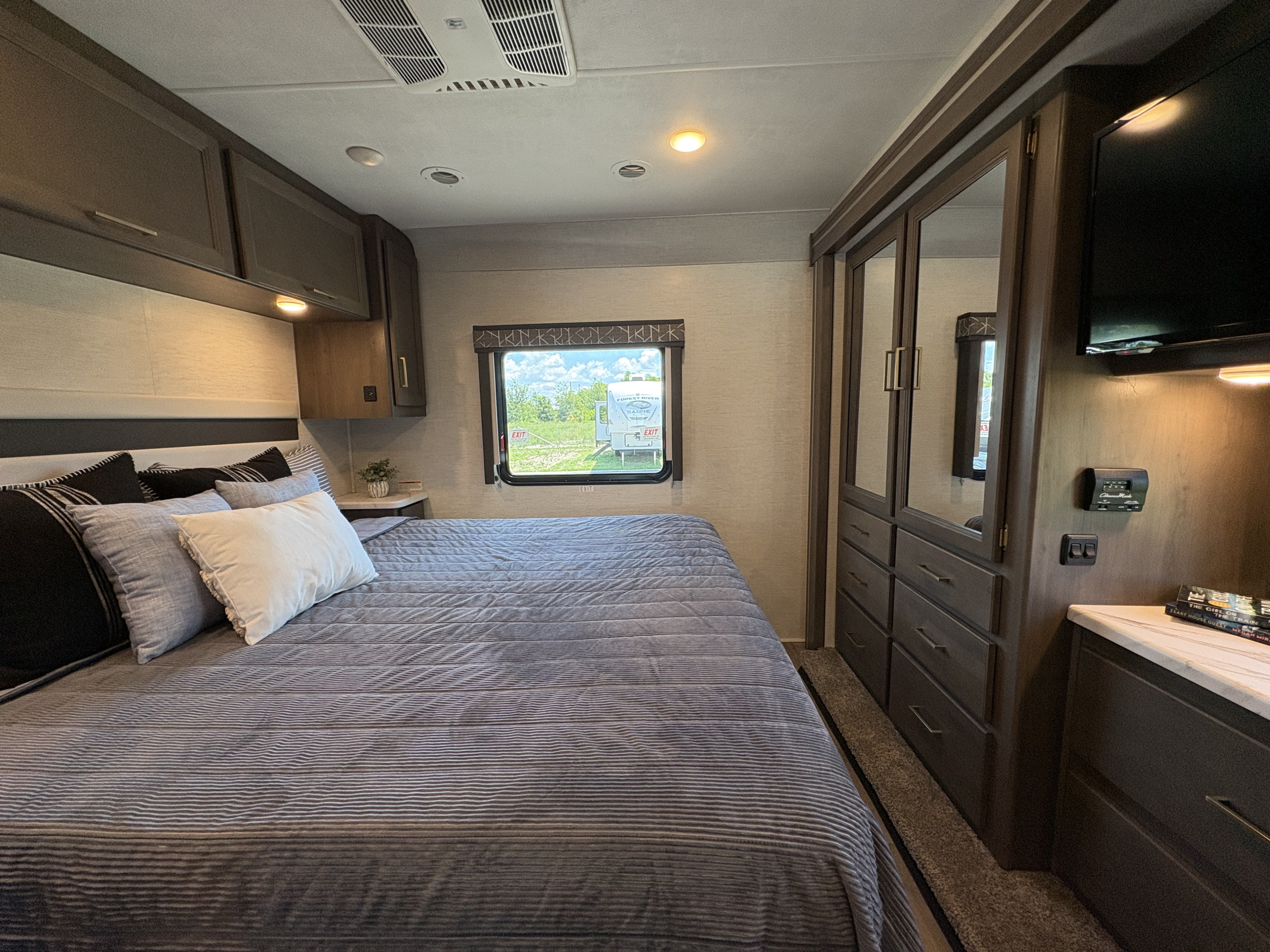 Experience comfort in this RV rental bedroom. Features a large bed, ample storage, TV, and a view into an RV park.. Thor ACE 2024