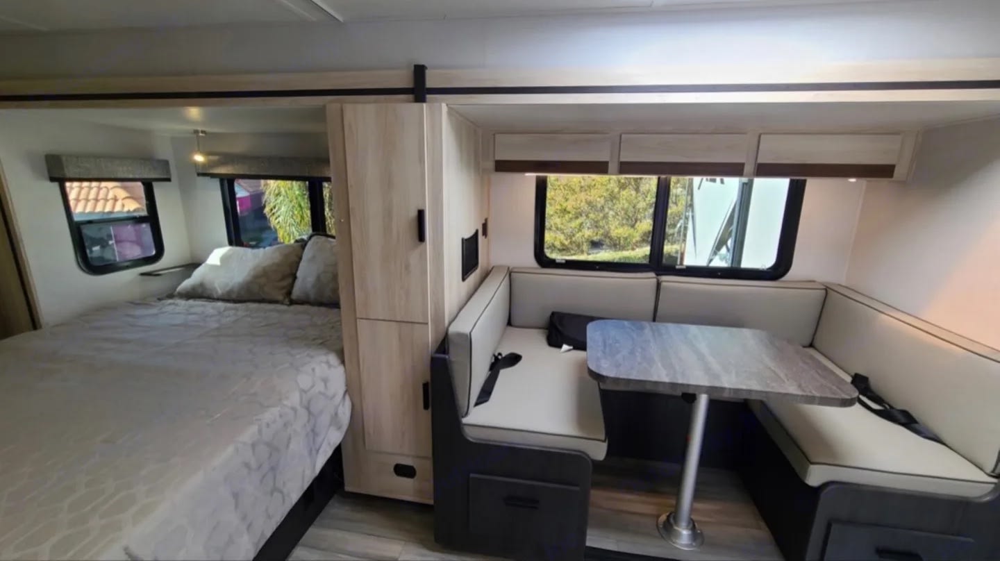 RV rental interior featuring a cozy bed on the left and a comfortable dinette with a table and bench seating on the right.. Forest River Forester 2023