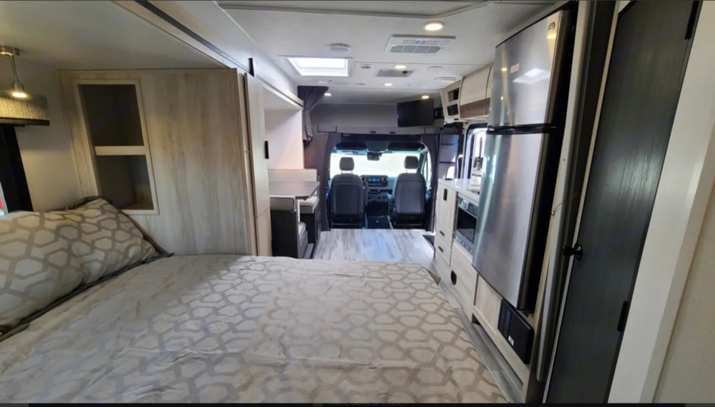 Explore this RV rental: a spacious interior showcasing a comfortable bed, full kitchen, dinette, and front cockpit area.. Forest River Forester 2023