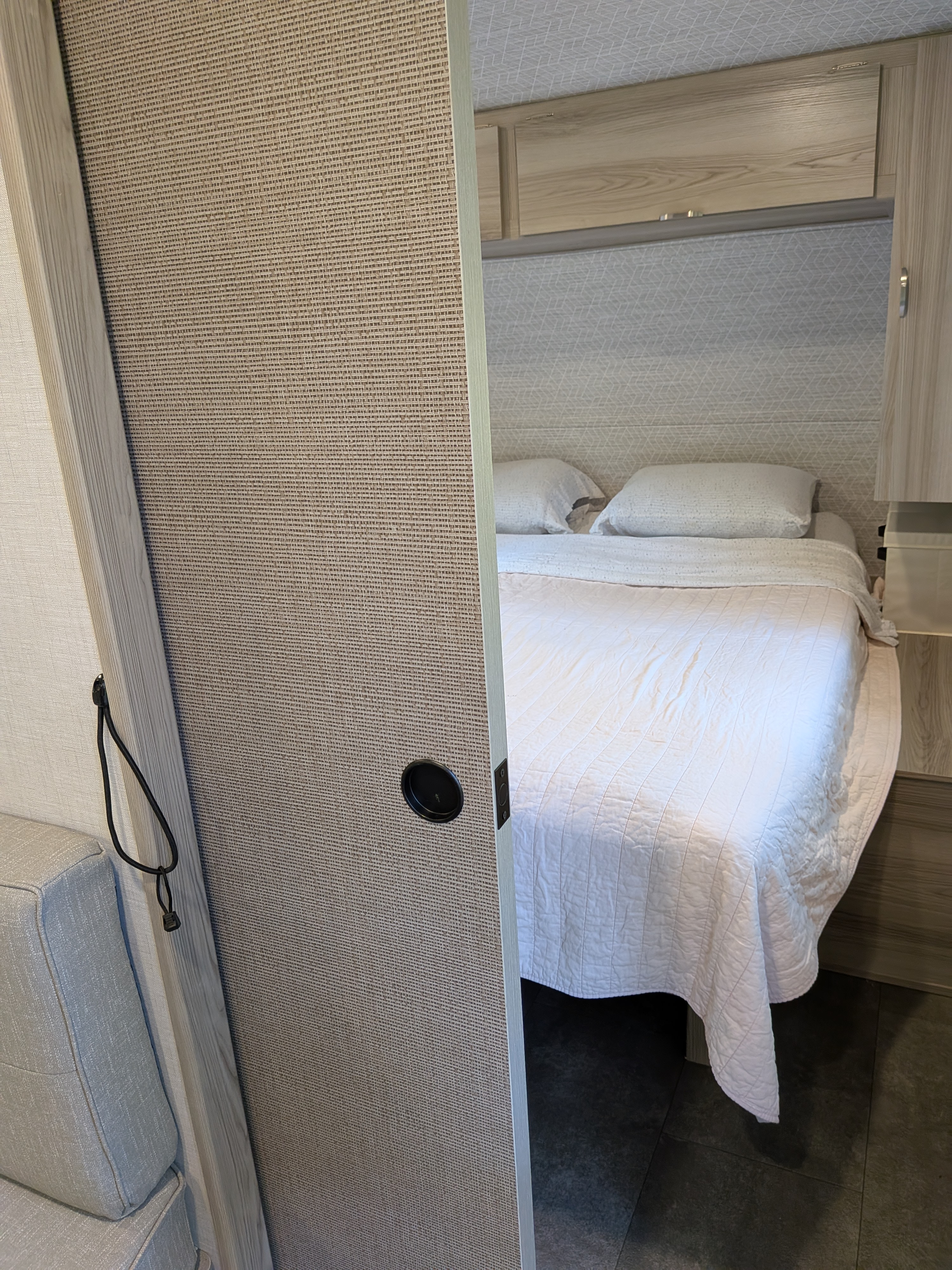 RV rental bedroom with a white bed, patterned wall, and overhead storage, visible through a textured sliding door.. Forest River Salem FSX 266BHLE 2025