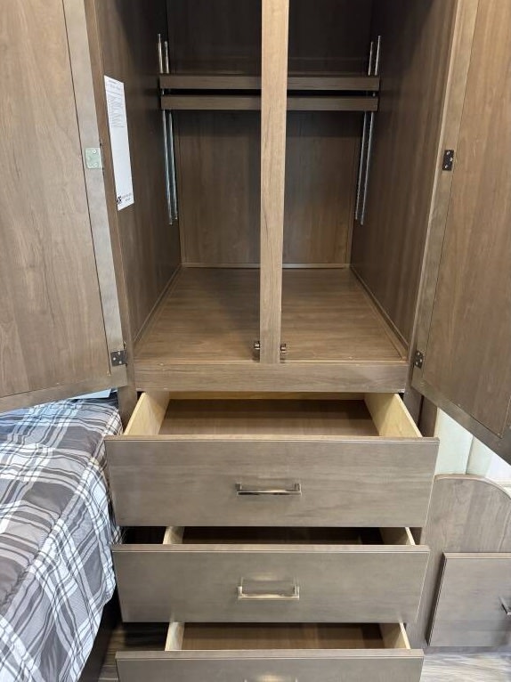 RV rental bedroom storage: open wardrobe with hanging rods & three open drawers next to a bed, showing ample space.. Thor Freedom Elite 2020