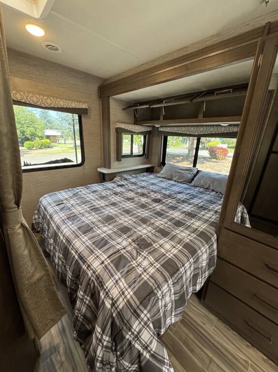 Comfortable RV rental bedroom featuring a plaid bed, multiple windows, and built-in storage. Ideal for travel accommodation.. Thor Freedom Elite 2020