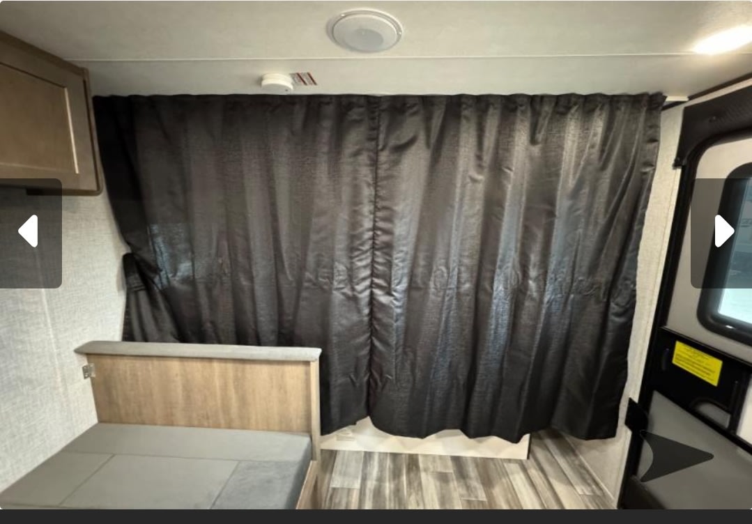 RV rental interior: Dark curtain covers a bed area with a wood cabinet and gray cushions, ideal for privacy.. Jayco Jay Flight SLX 2025