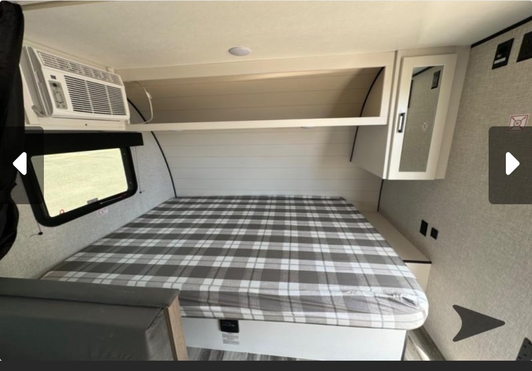 Inside this RV rental: a compact bedroom with a plaid bed, window, AC unit, and overhead storage.. Jayco Jay Flight SLX 2025
