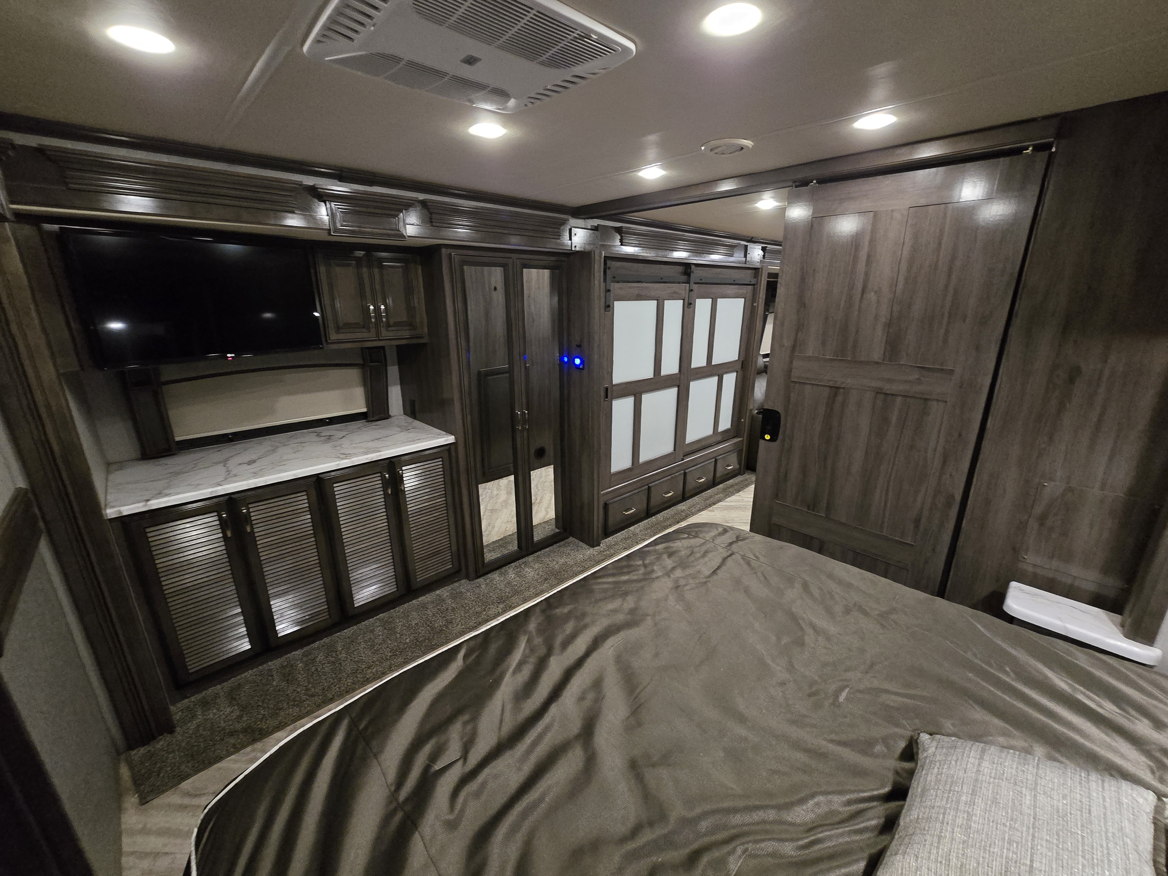 Modern RV rental bedroom featuring built-in TV, marble-look counter, ample cabinets, and sliding closet doors for compact living.. Holiday Rambler Navigator 2020