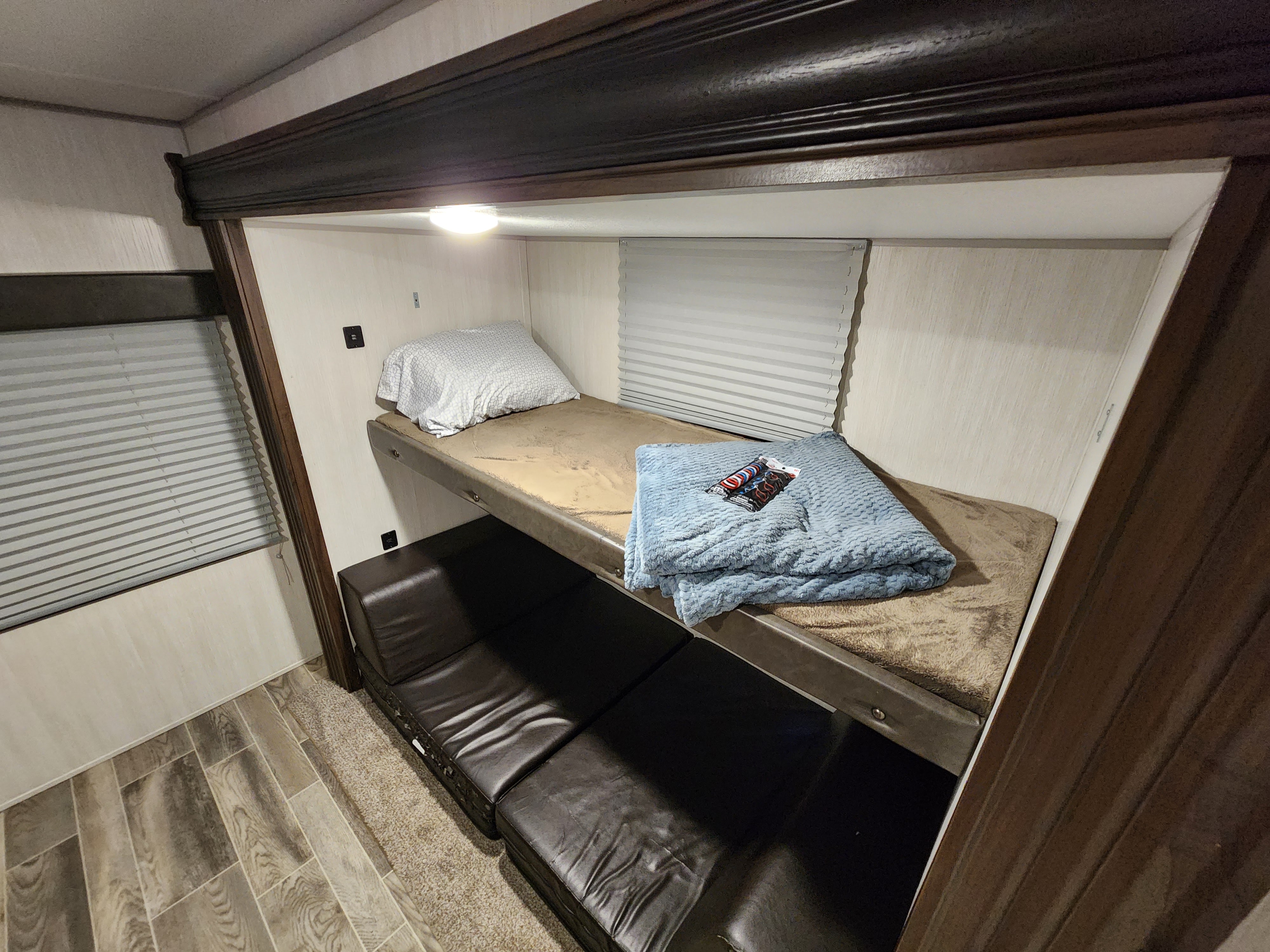 Inside an RV rental: cozy bunk beds with light, window blinds, and lounge space below.. Forest River Cherokee 2019