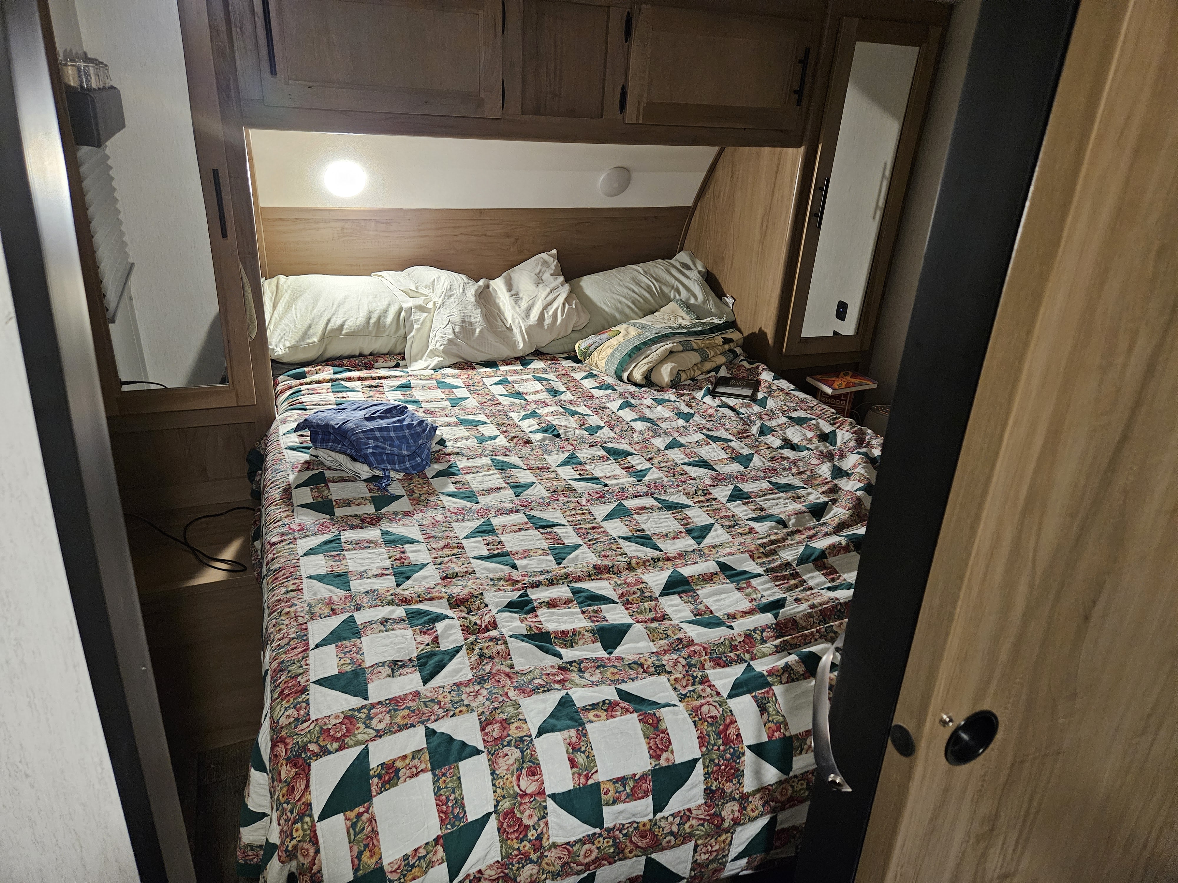 Cozy RV rental bedroom with a floral quilt, overhead cabinets, and built-in lighting, perfect for travel comfort.. Forest River Cherokee 2023