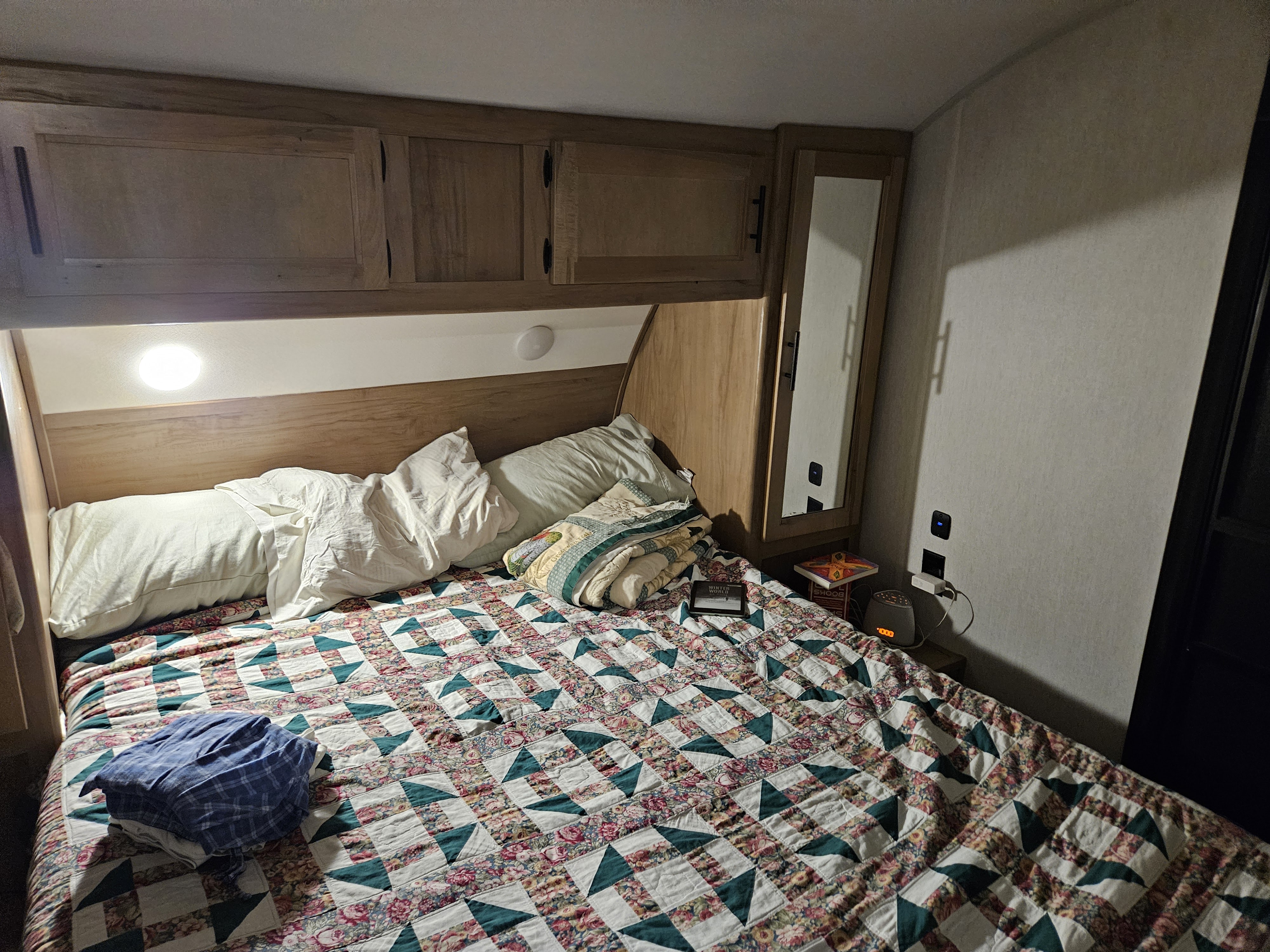 Inside an RV rental: a cozy bedroom with a patterned quilt, overhead storage, and bedside electronics.. Forest River Cherokee 2023