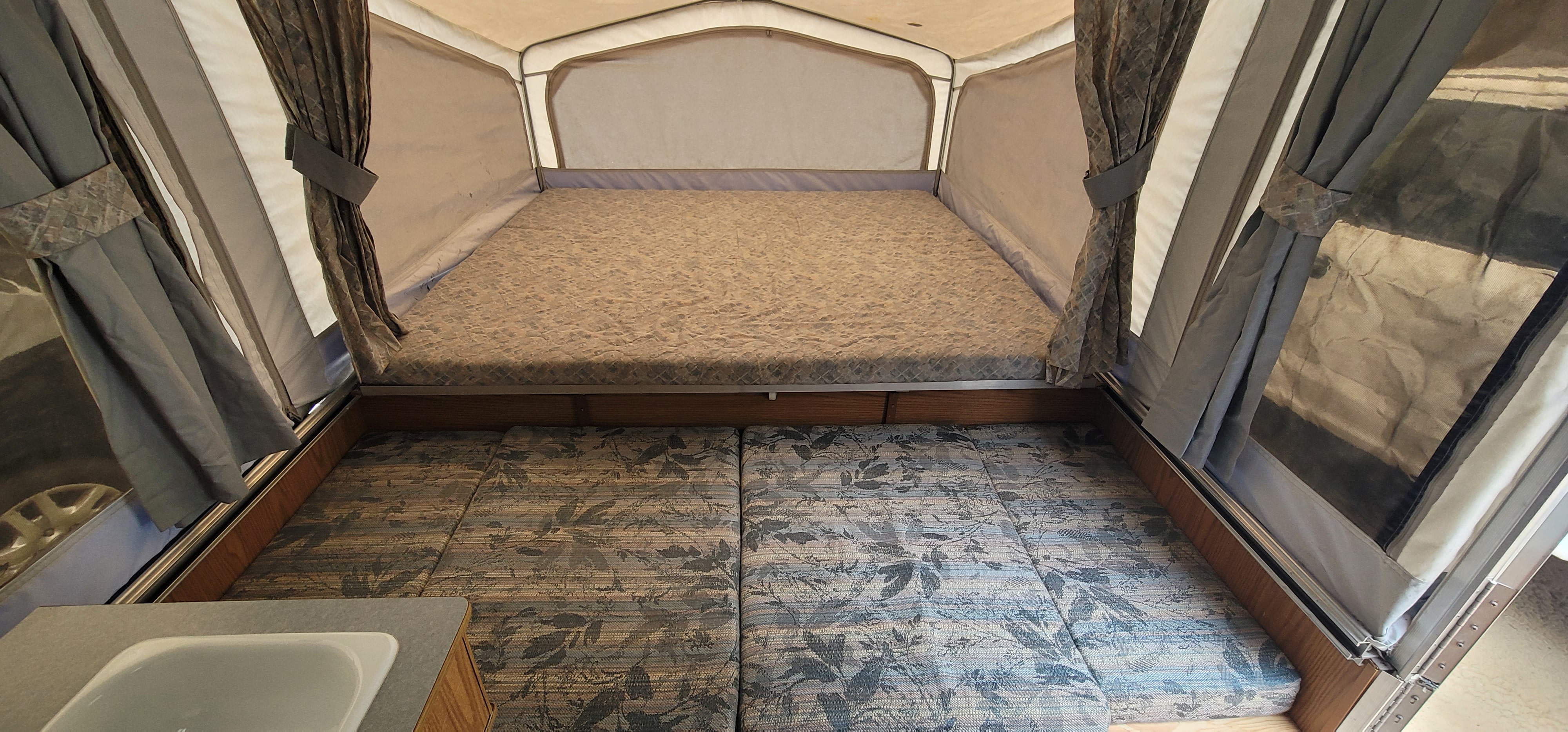 RV rental pop-up camper interior, showing a cozy bed, patterned seating, and a partial sink. Perfect for camping!. Starcraft Starcraft Popup Trailer 2002