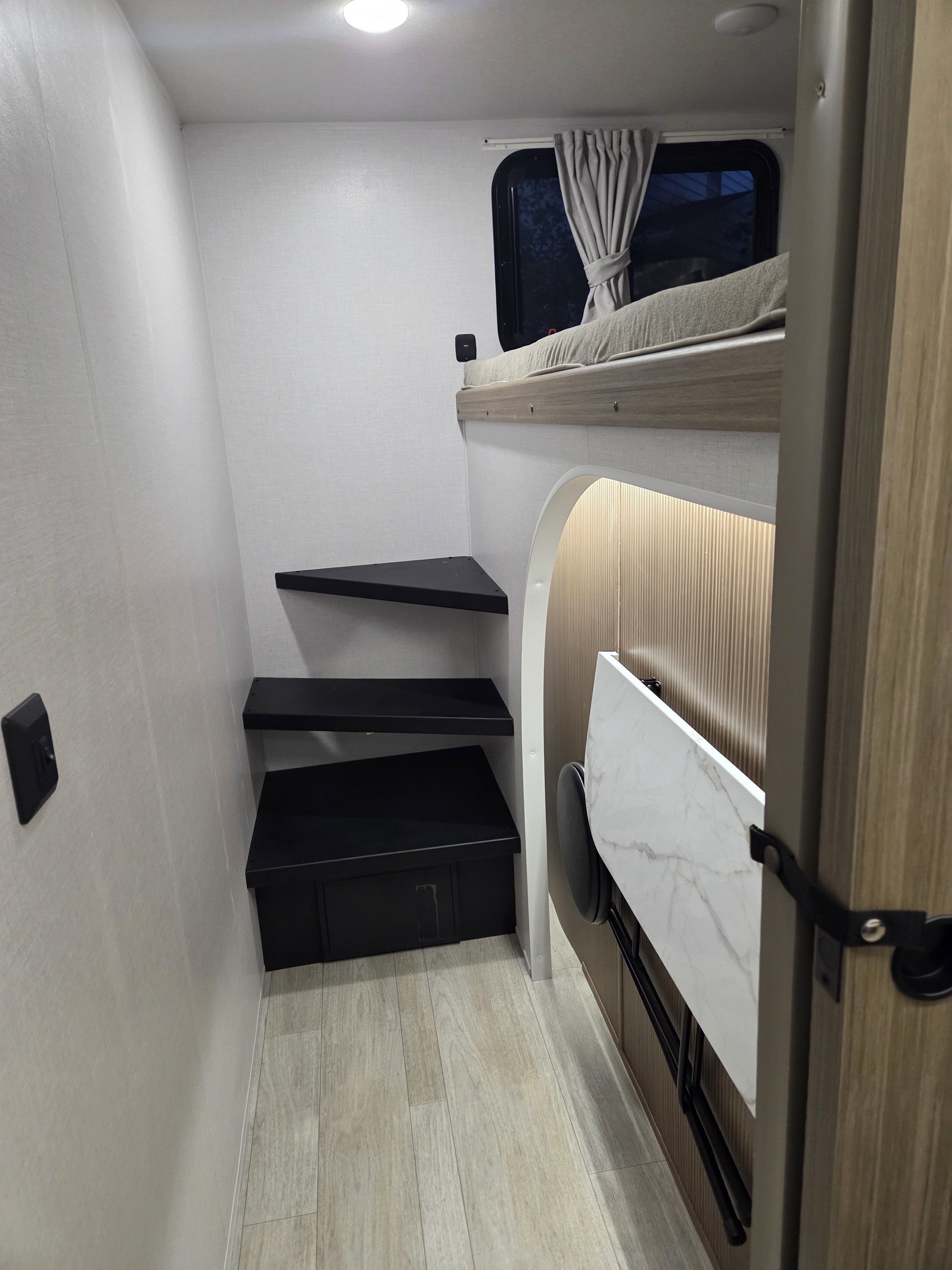 Inside an RV rental: a bunk bed with window, clever modular steps, and a fold-away table with stool,. Forest River Wildwood 2026