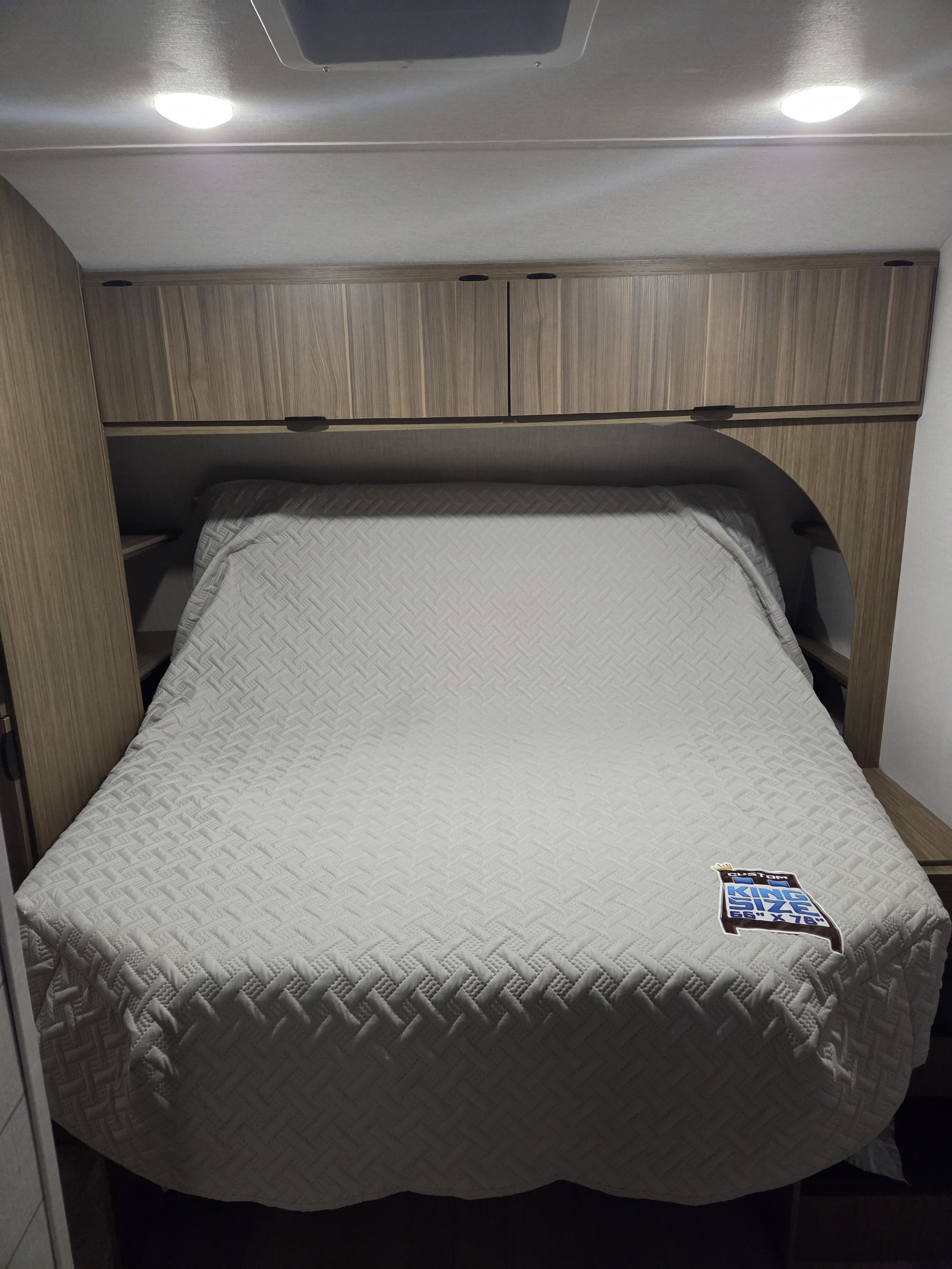 Brightly lit RV rental bedroom featuring a quilted custom king-size bed (66"x78") and integrated overhead storage.. Forest River Wildwood 2026