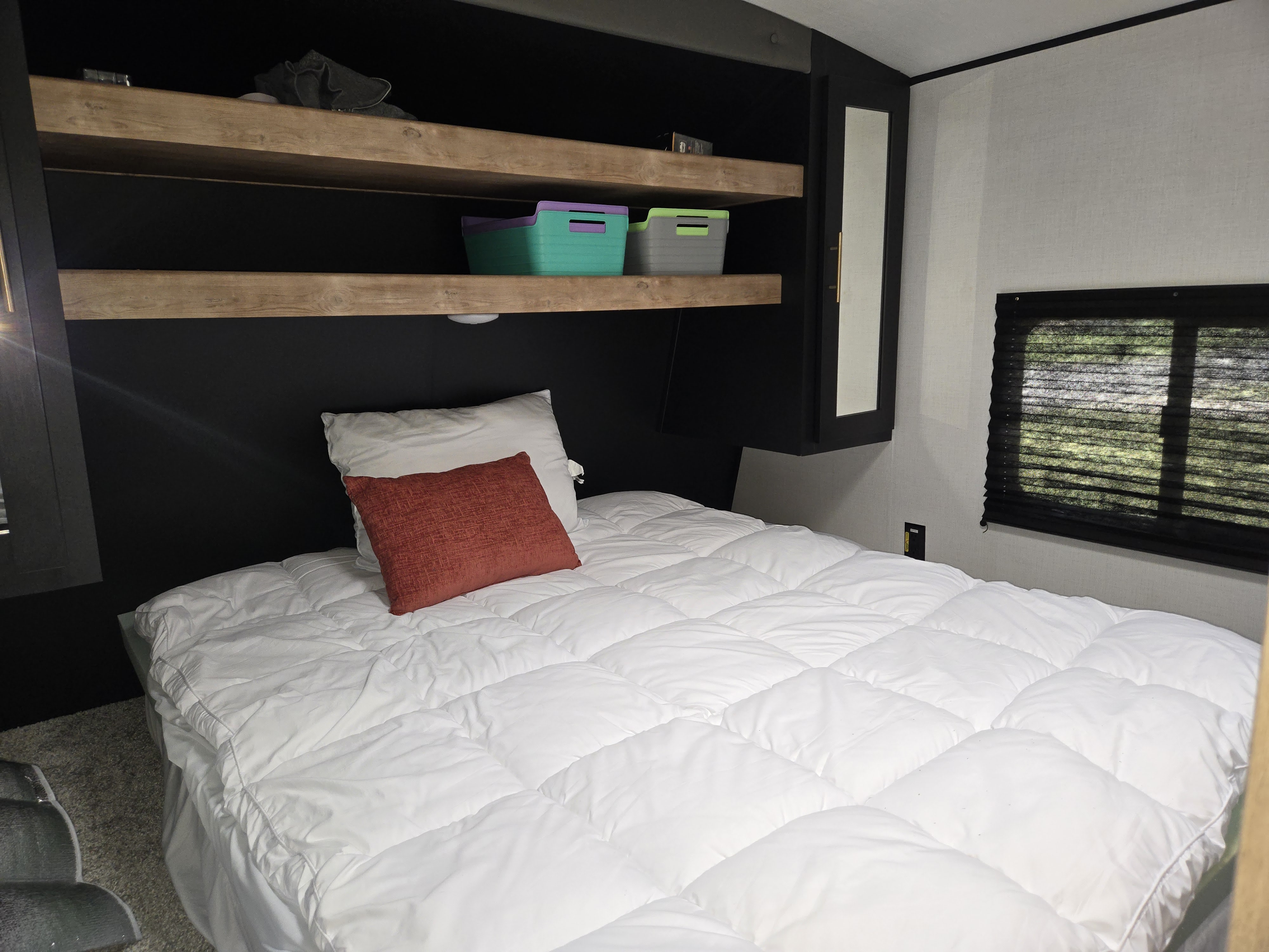 Cozy RV rental bedroom with a comfy white bed, dark accent wall, wooden shelves with storage, and. Keystone RV Springdale 2023