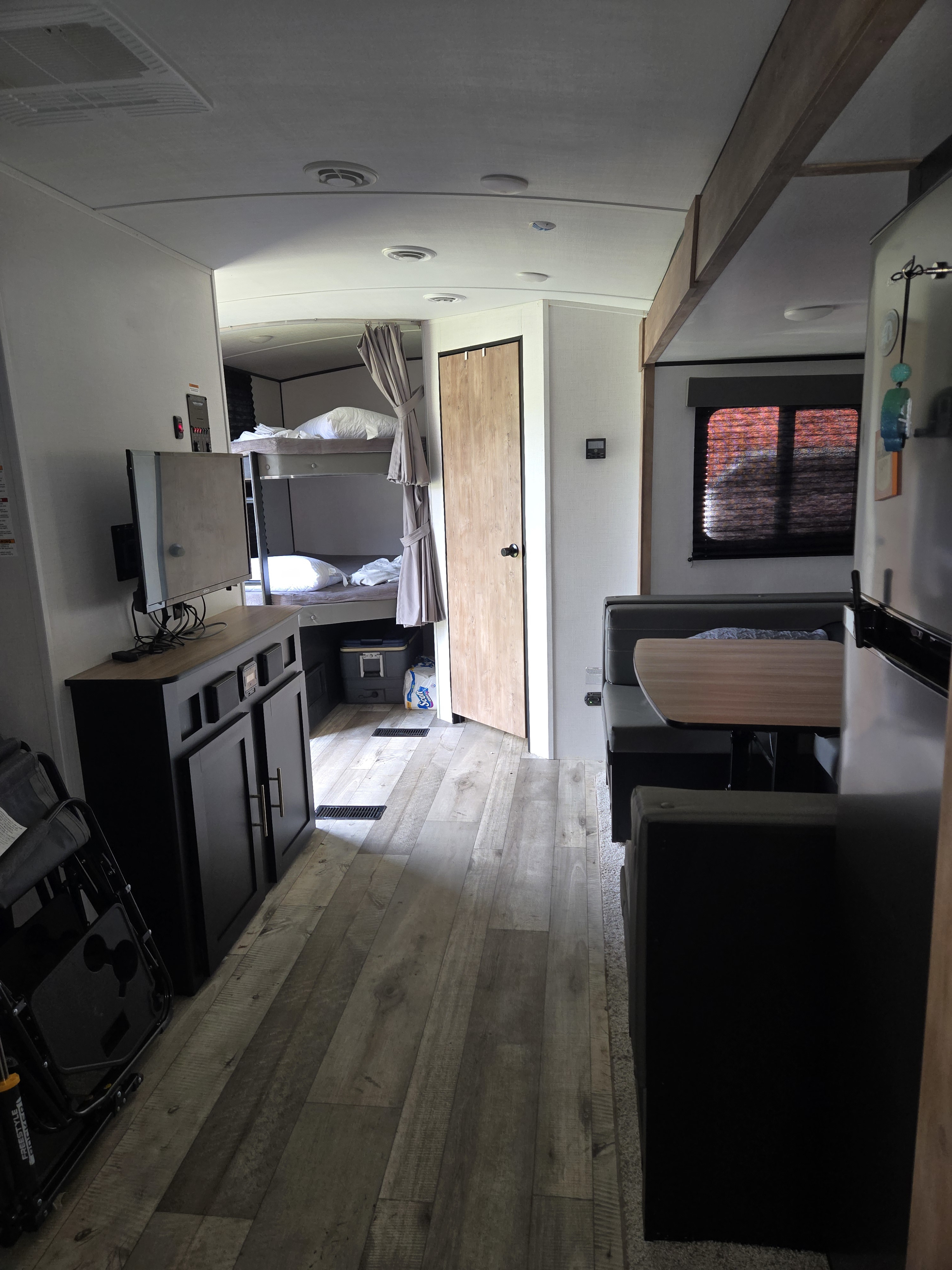 Inside an RV rental, showing bunk beds, a dinette, TV console, and wood-look flooring, creating a cozy living space.. Keystone RV Springdale 2023