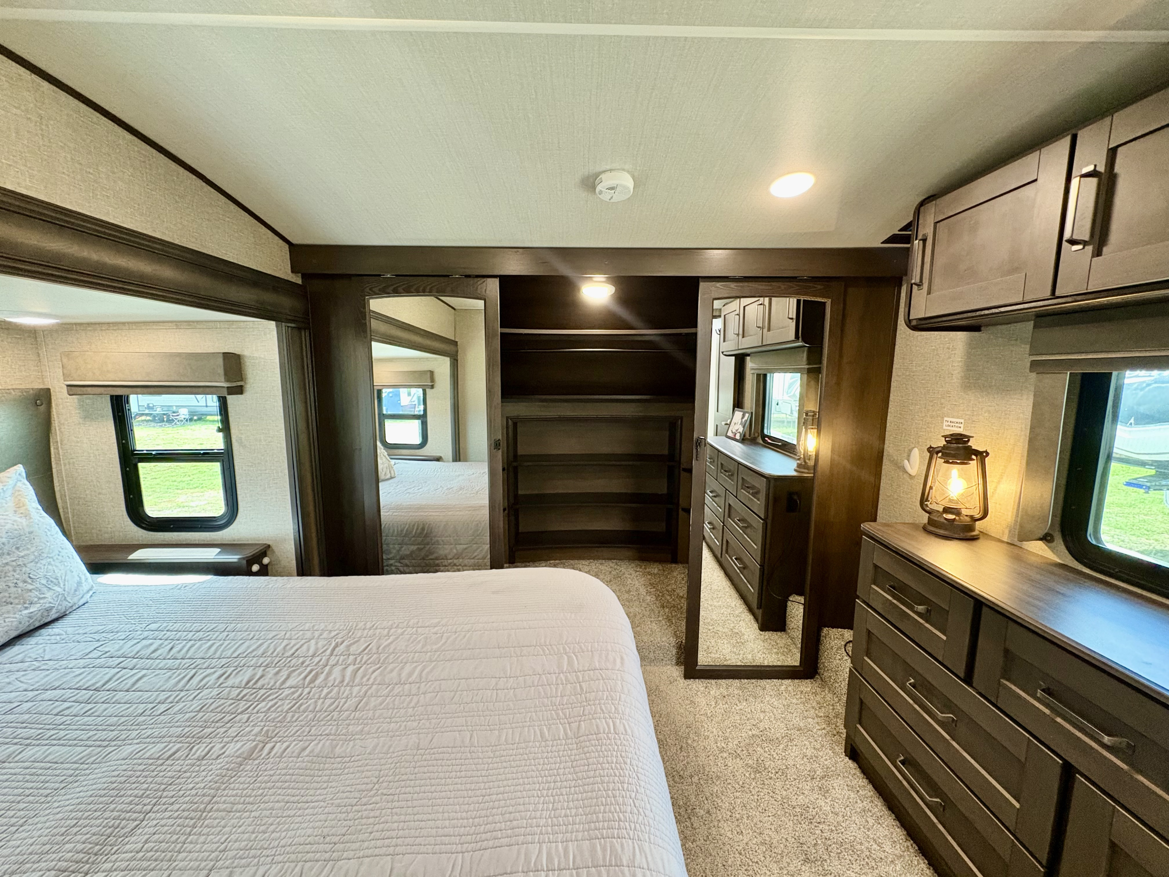 Bright RV rental bedroom showcasing a comfortable bed, dresser, and mirrored closet. Ideal for travel trailer stays.. Grand Design Reflection 2022