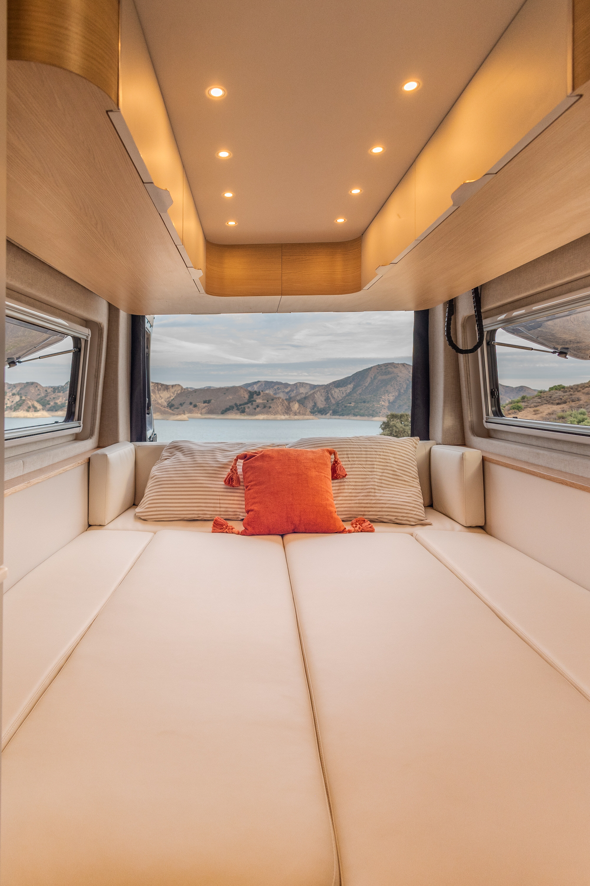 Enjoy this RV rental's cozy bed and scenic view! A comfortable light wood interior with windows overlooking a lake and mountains.. Noovo Plus LB 2025