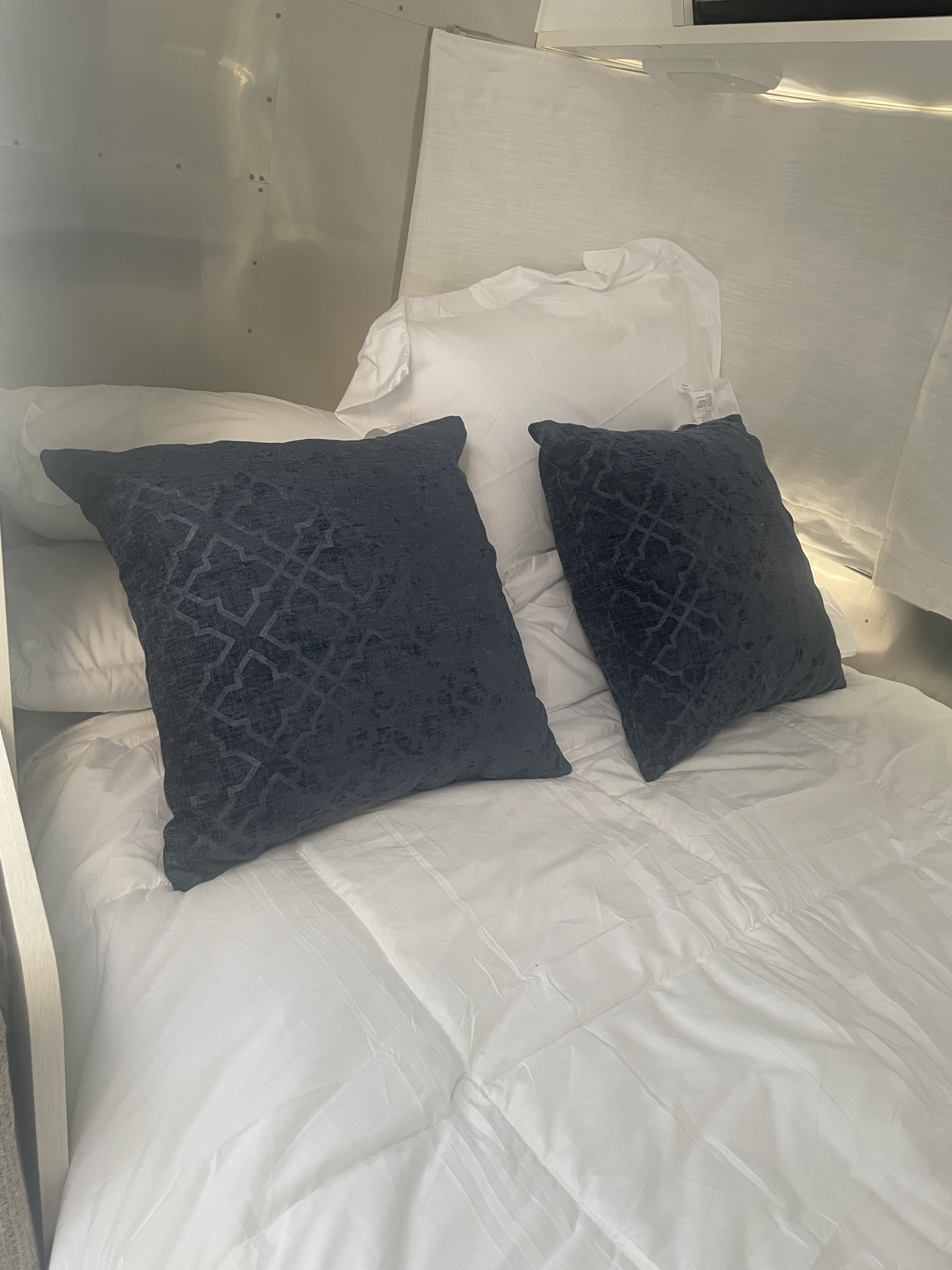 Comfortable RV rental sleeping area featuring crisp white bedding and two decorative blue patterned pillows.. Airstream Bambi 2020