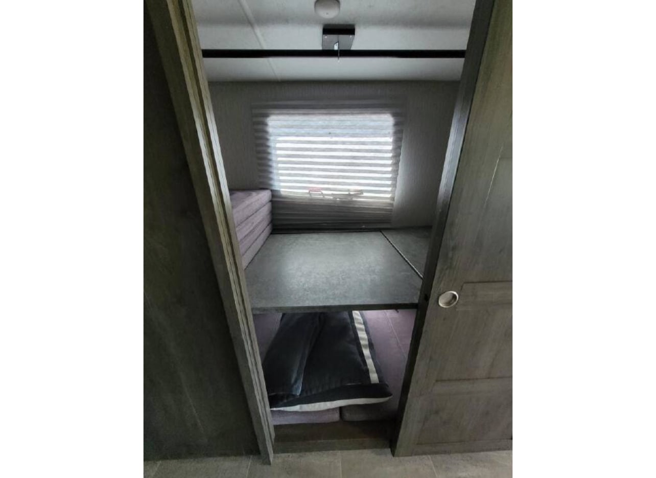 Cozy RV rental bunk room showing upper and lower sleeping levels, a window with blinds, and stacked cushions.. Forest River Coachmen Mirada 2022