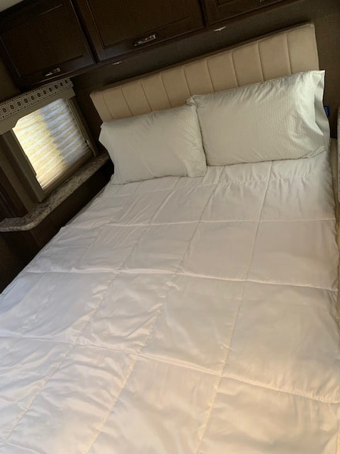 Step inside your cozy RV rental bedroom! Features a neatly made bed with fresh white linens & pillows, ideal for comfortable travel.. Thor Four Winds 2017