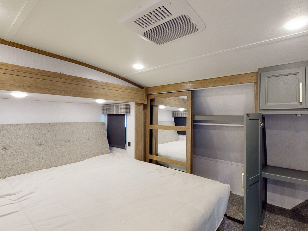 RV rental bedroom interior featuring a spacious bed, built-in storage, and a mirrored sliding closet door.. Keystone RV Eddie Bauer Signature 360LF 2024