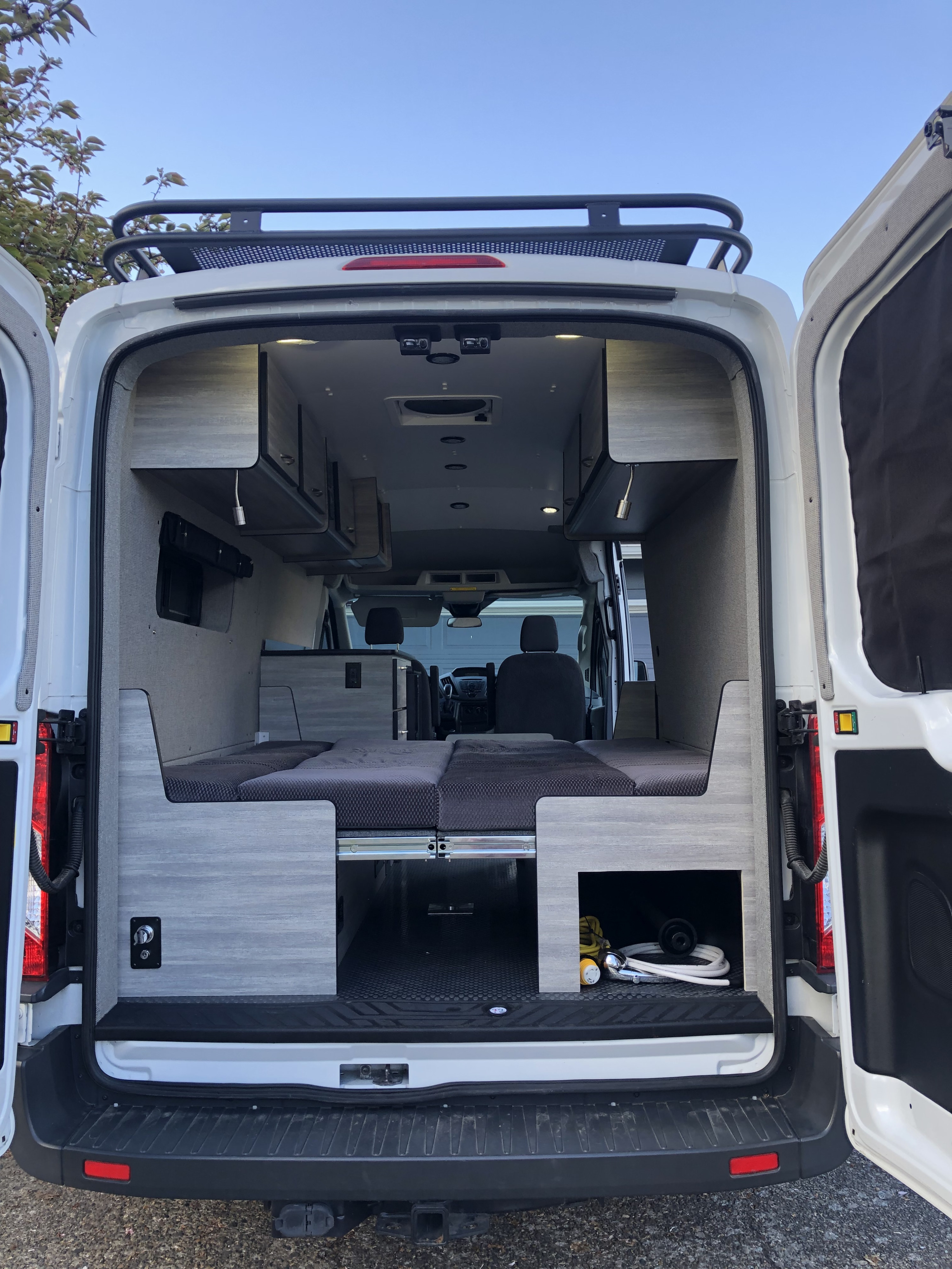Discover this versatile RV rental: a modern camper van interior with modular bed, ample storage, and a roof rack.. Ford Transit 2017