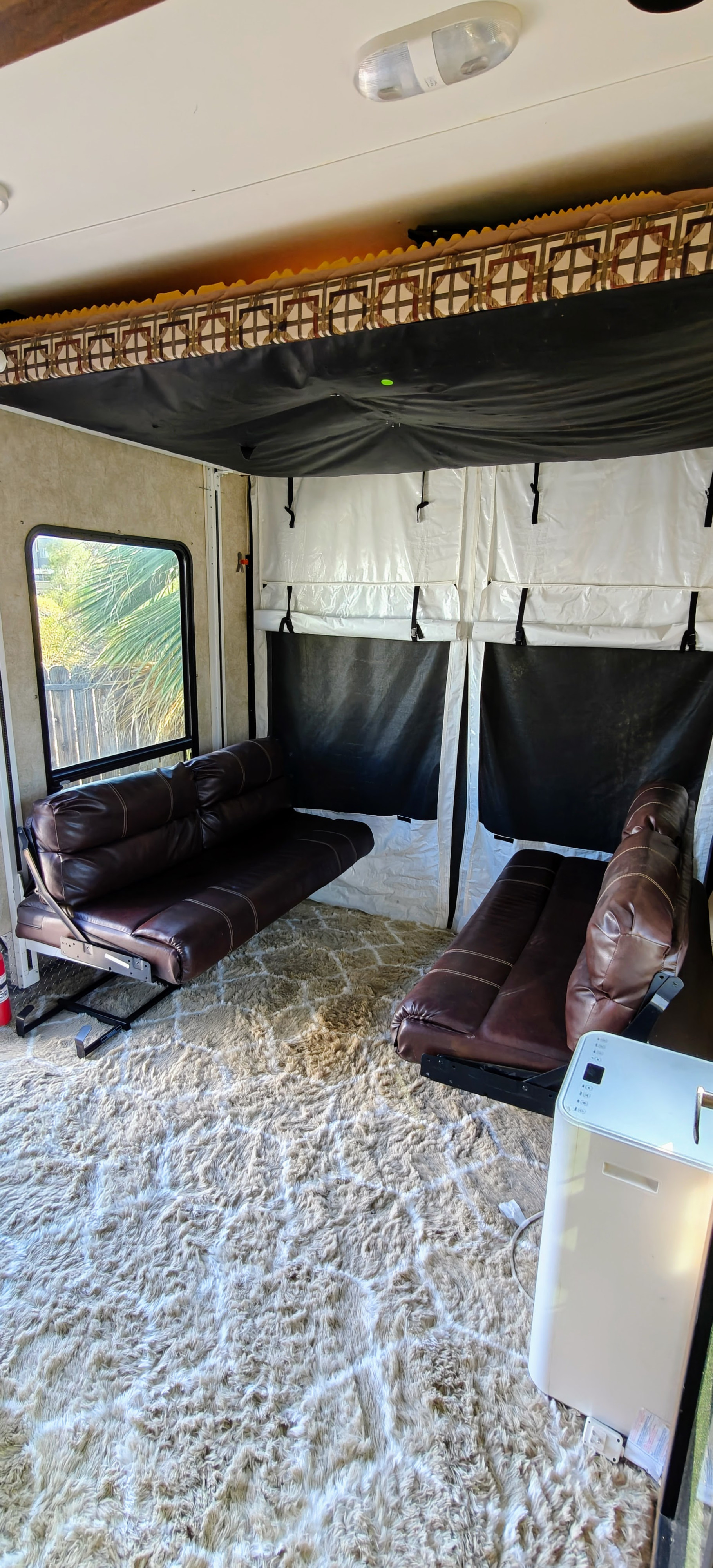 Inside an RV rental: a comfortable toy hauler living space with plush rug, two brown leather couches, and a portable AC unit.. Keystone Carbon 2015