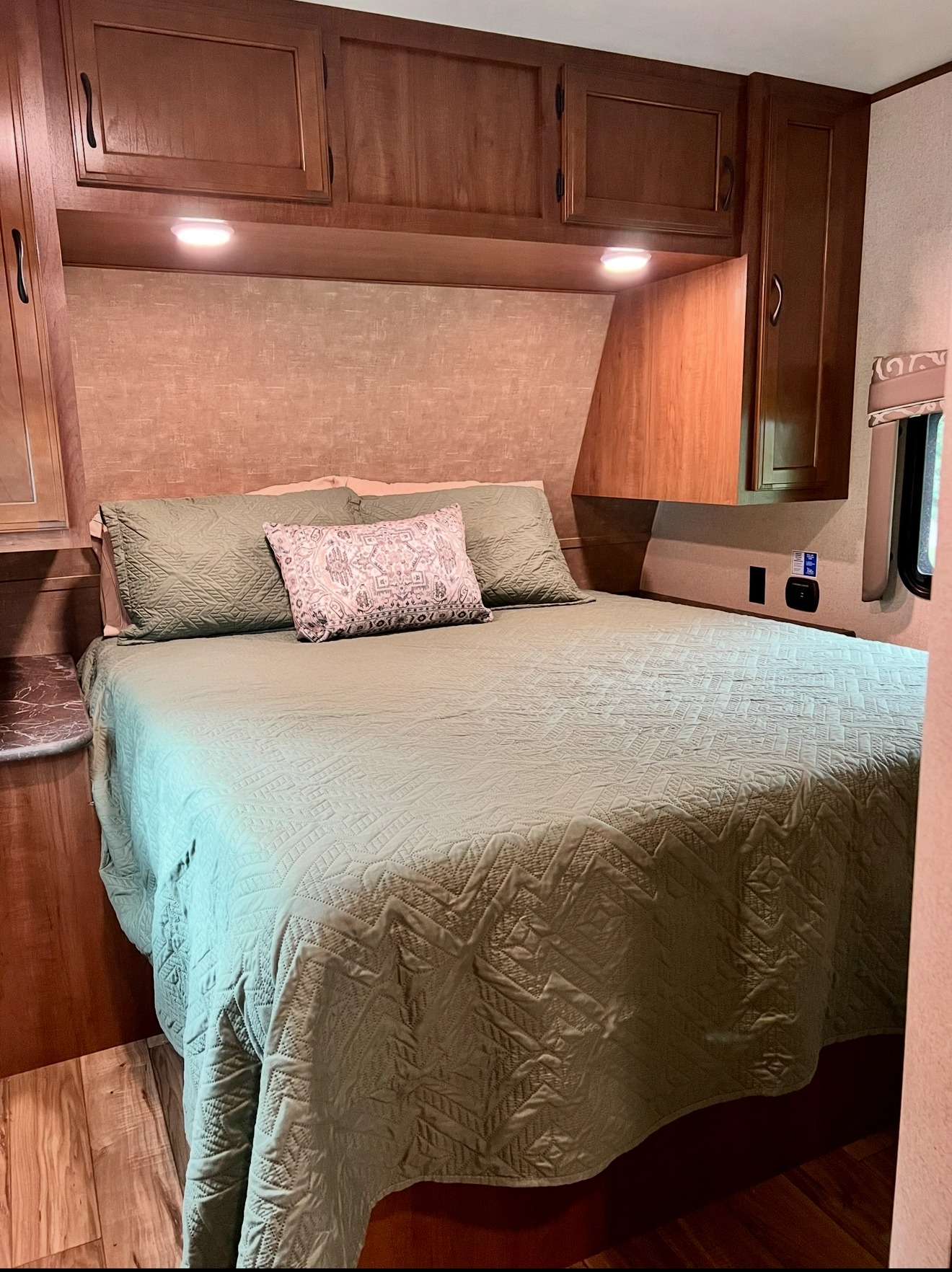 Inside an RV rental bedroom showing a bed with a green quilted comforter, patterned pillow, and wood storage cabinets.. Jayco Jay Flight 2016