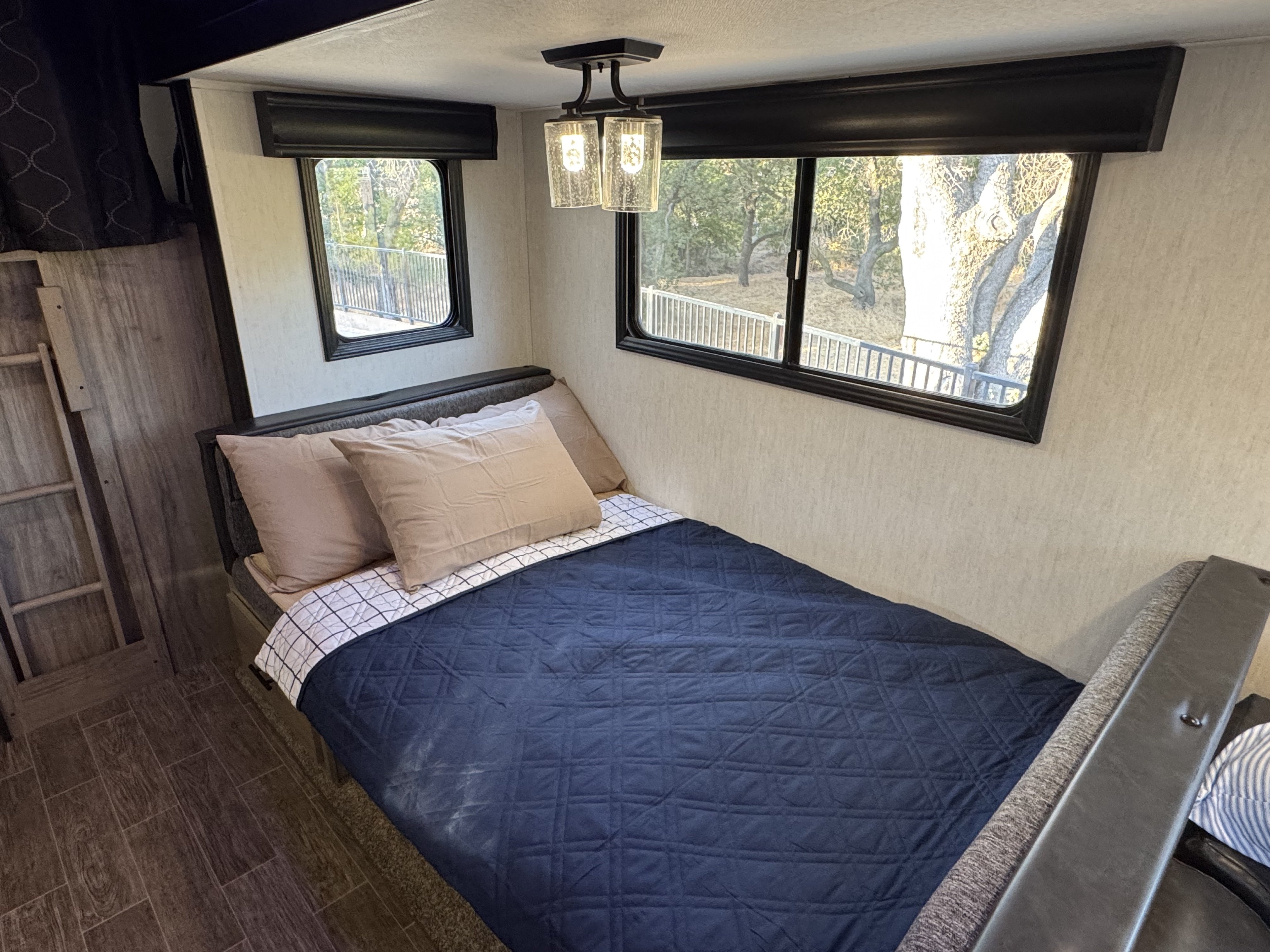 Comfortable RV rental bedroom featuring a bed, ample windows with an outdoor view, ceiling light, and ladder access.. Forest River Cherokee Alpha Wolf 2022