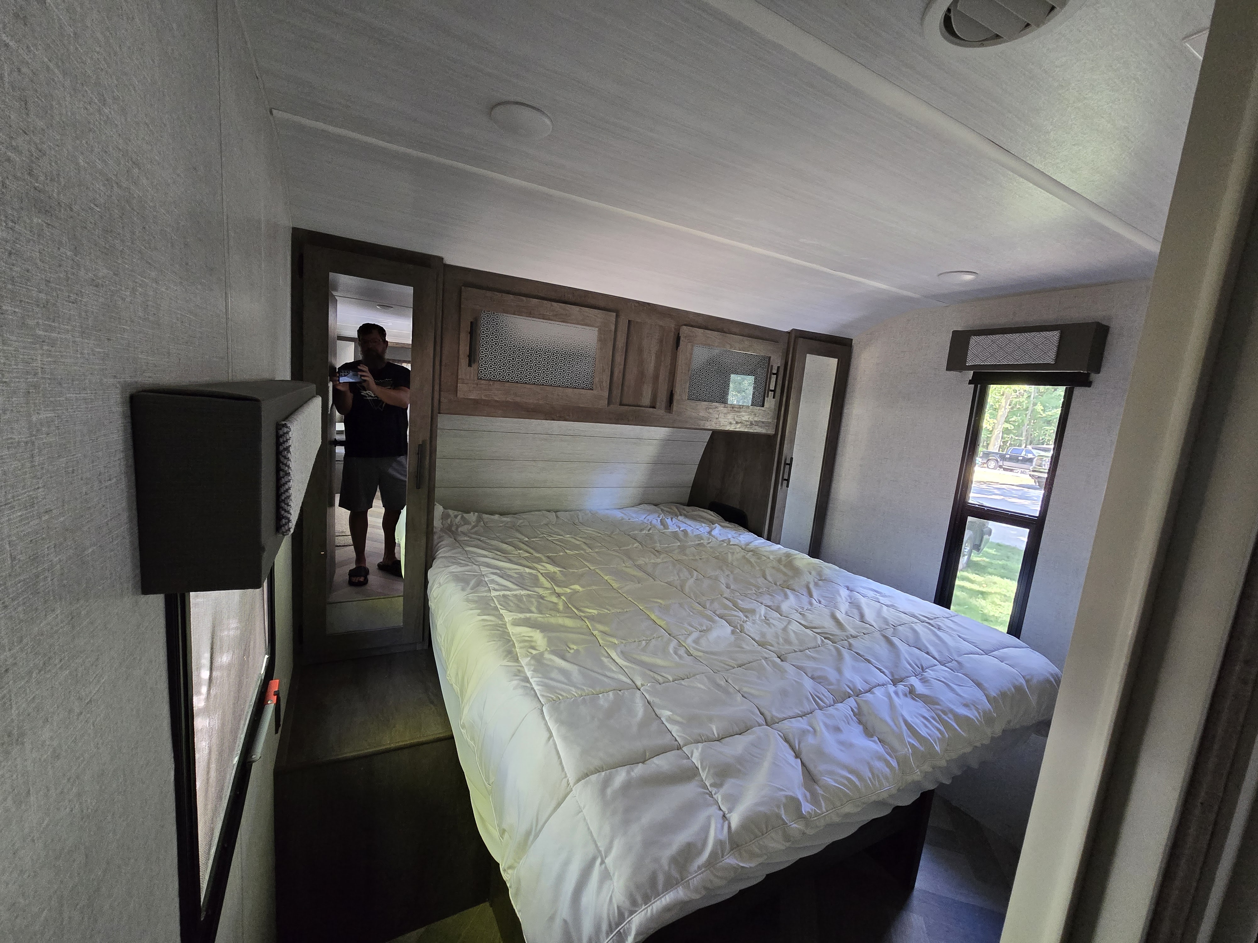 Spacious RV bedroom with a comfy bed, ideal for an RV rental adventure. Reflected person in doorway.. Forest River Wildwood 2020