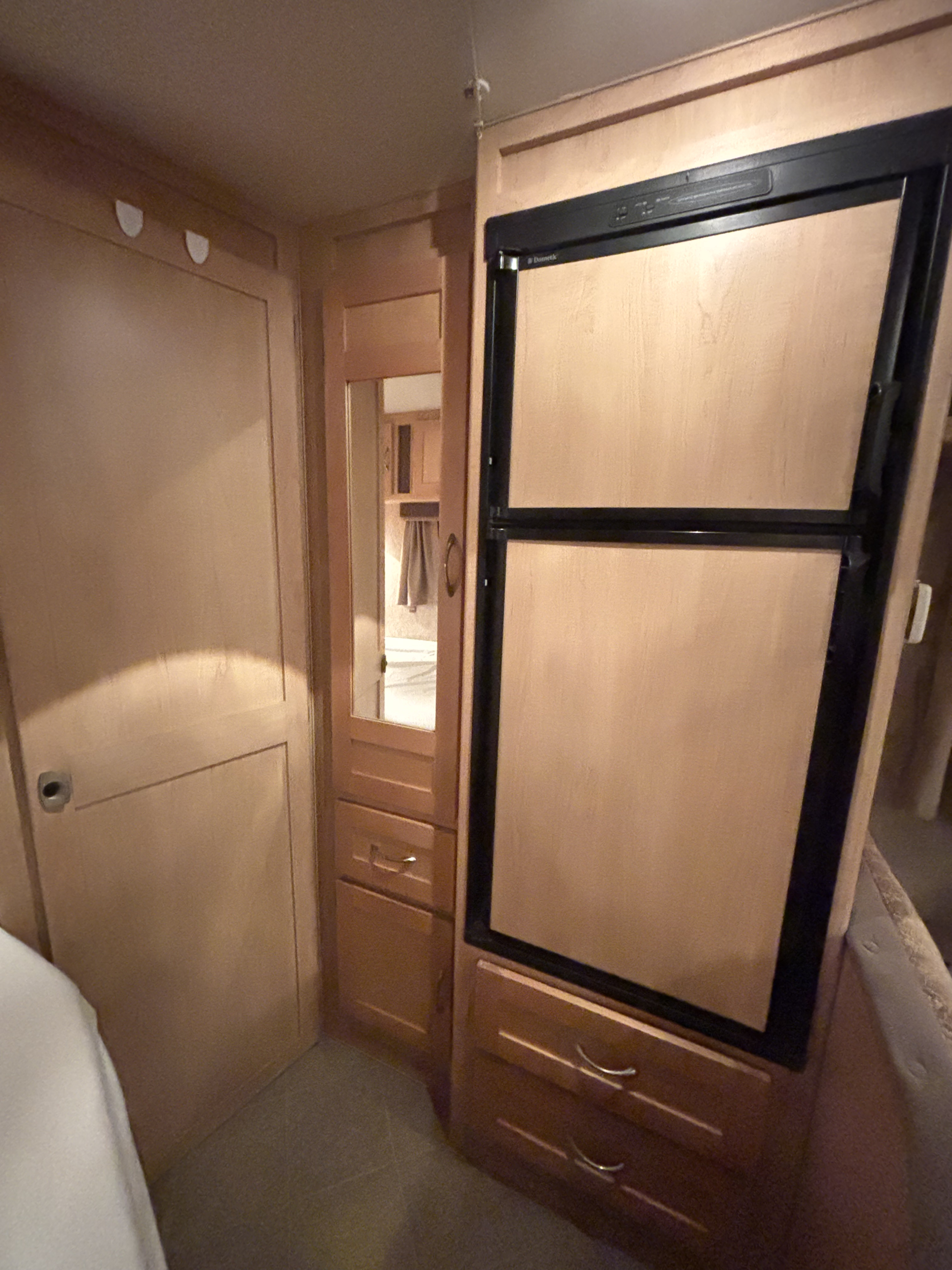 Wood paneled RV rental interior showing a Dometic fridge, storage cabinet with mirror, and closed door on the left.. Adventurer Adventurer Motorhome 2008