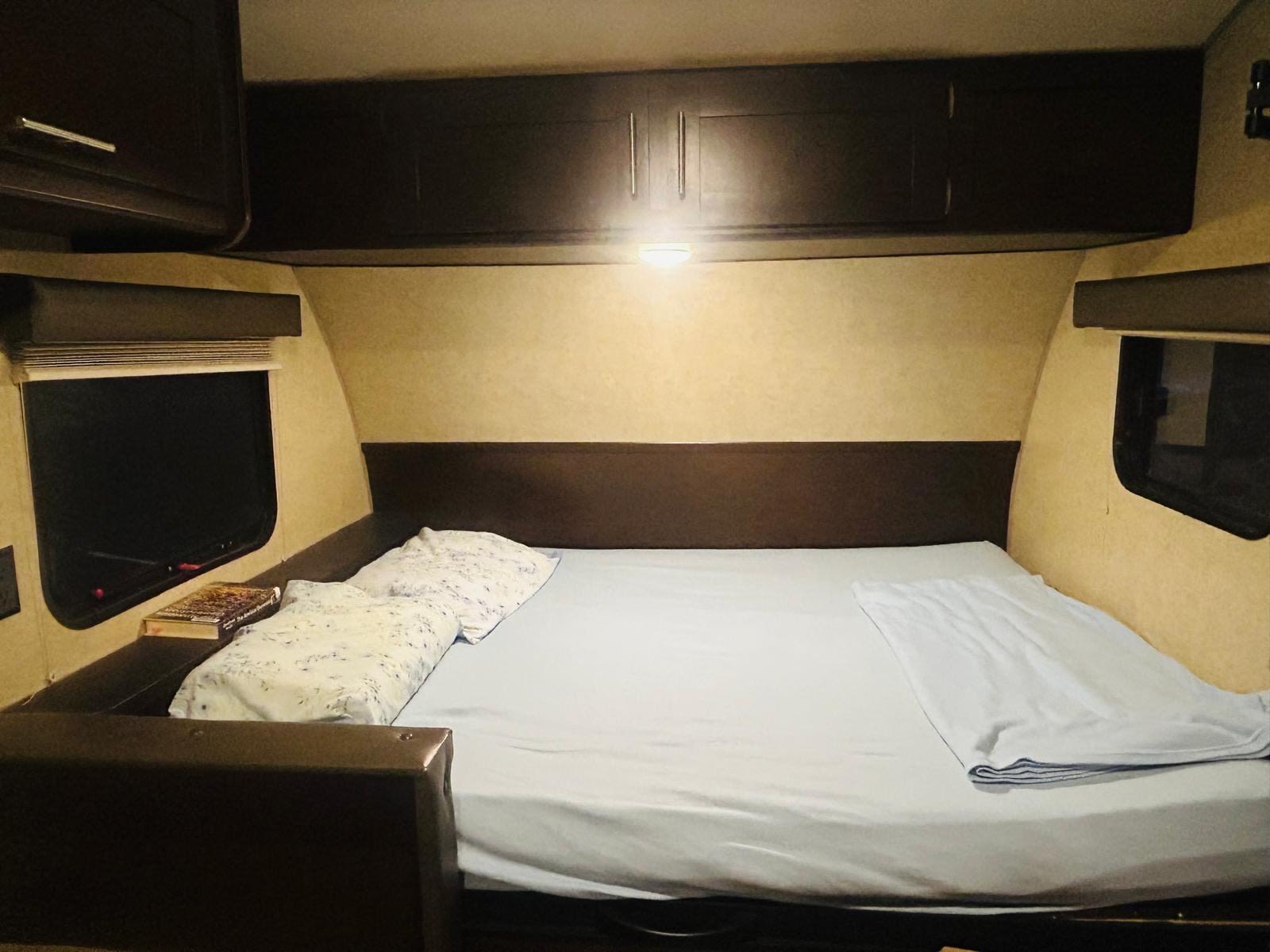 Cozy RV rental bedroom with a neatly made bed, overhead cabinets, and windows on both sides, ready for your trip.. Forest River Cherokee Wolf Pup Cascade 2017