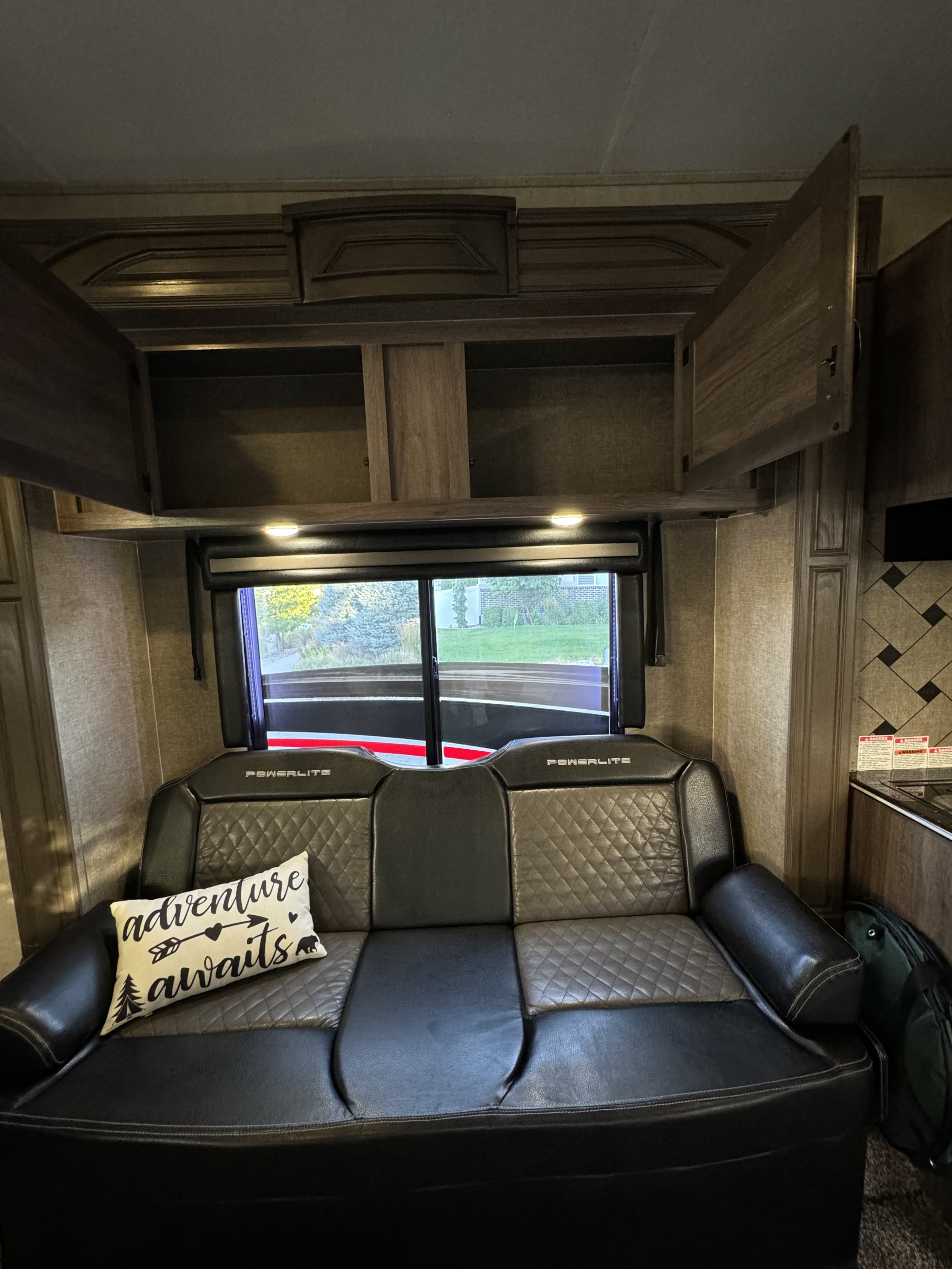 Inside an RV rental: A dark, diamond-patterned sofa, open wood cabinets, and large windows revealing outdoor scenery.. Pacific Coachworks Powerlite 2017