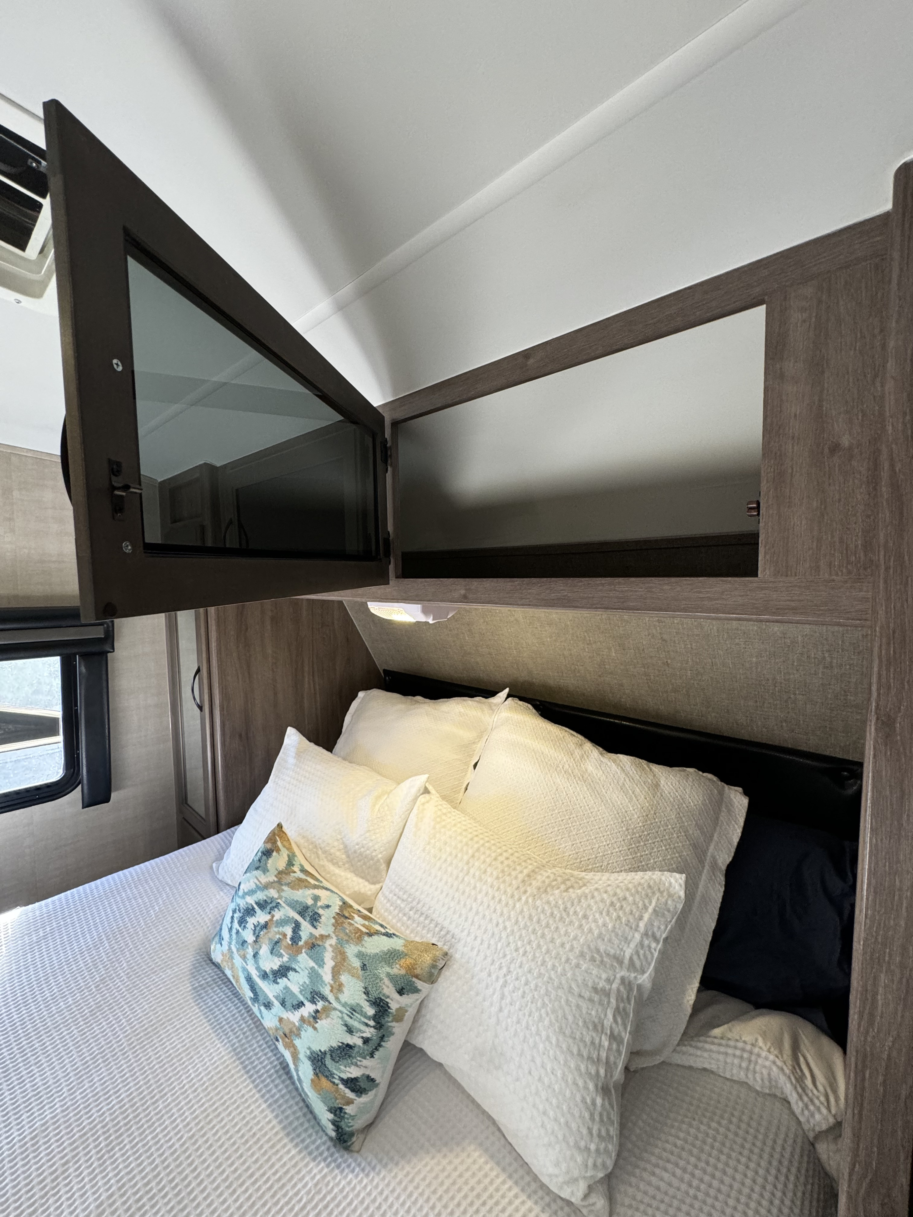 Comfortable RV rental bedroom featuring white bedding, an accent pillow, and convenient overhead storage.. Pacific Coachworks Powerlite 2017