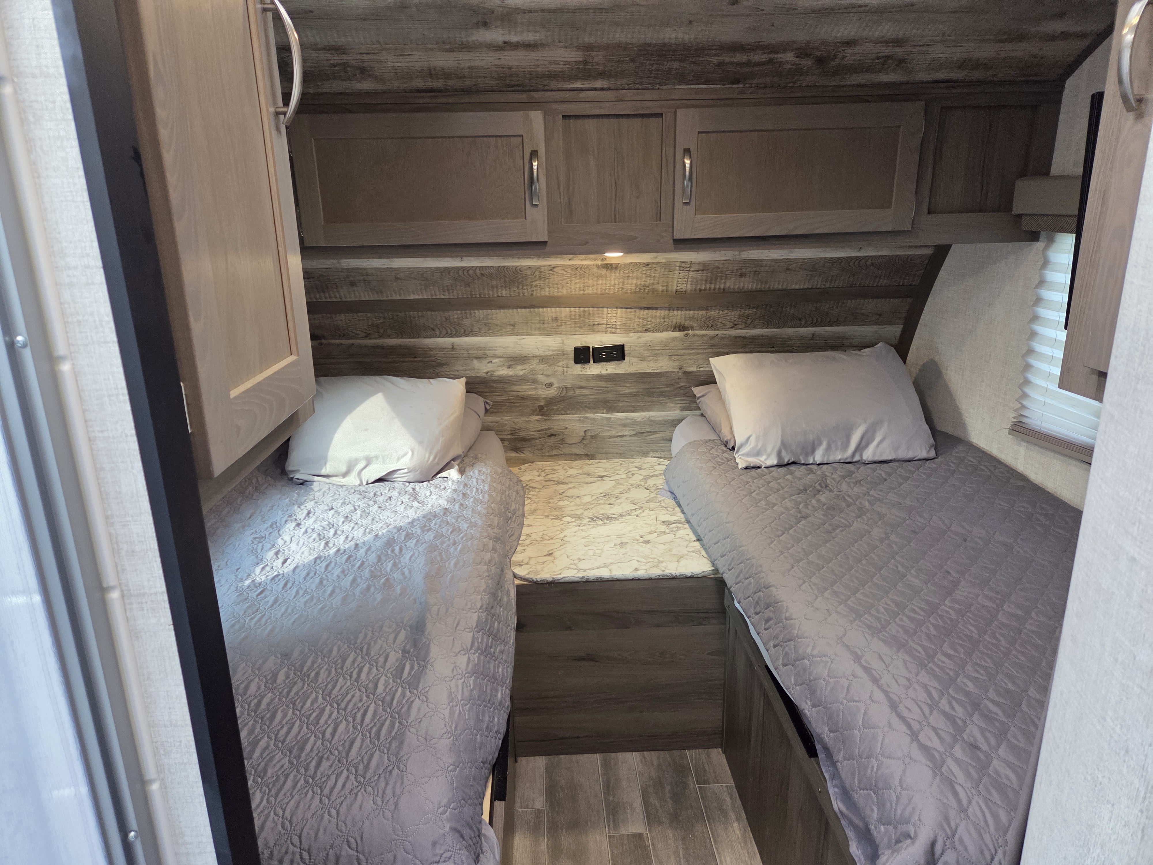 Cozy RV rental bedroom features twin beds with gray quilts, a central storage unit, and overhead cabinets.. Gulf Stream Vista Cruiser 2022