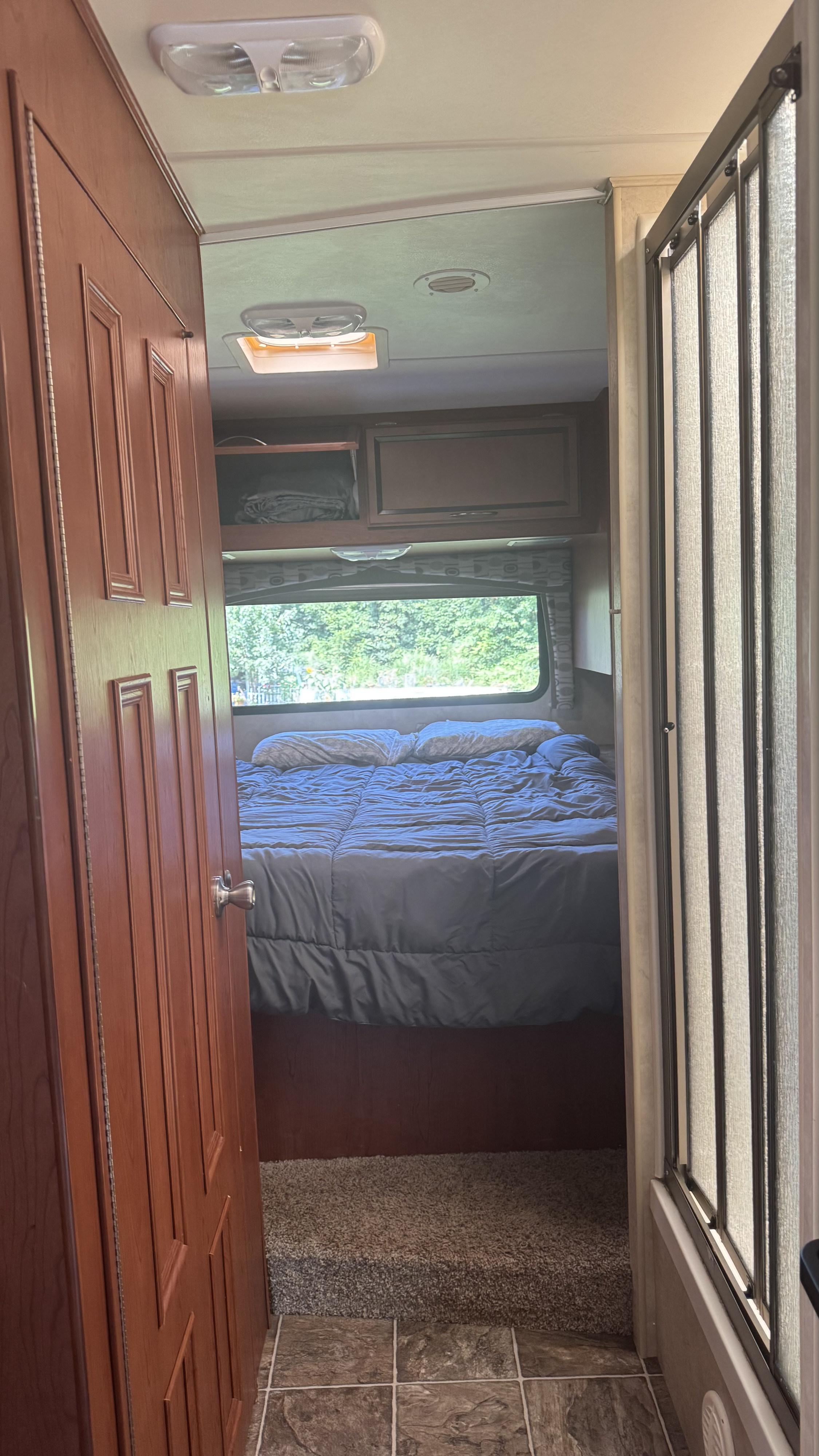 View from an RV rental's main area into the bedroom, showing a bed, overhead storage, and adjacent shower.. Thor Chateau 2012
