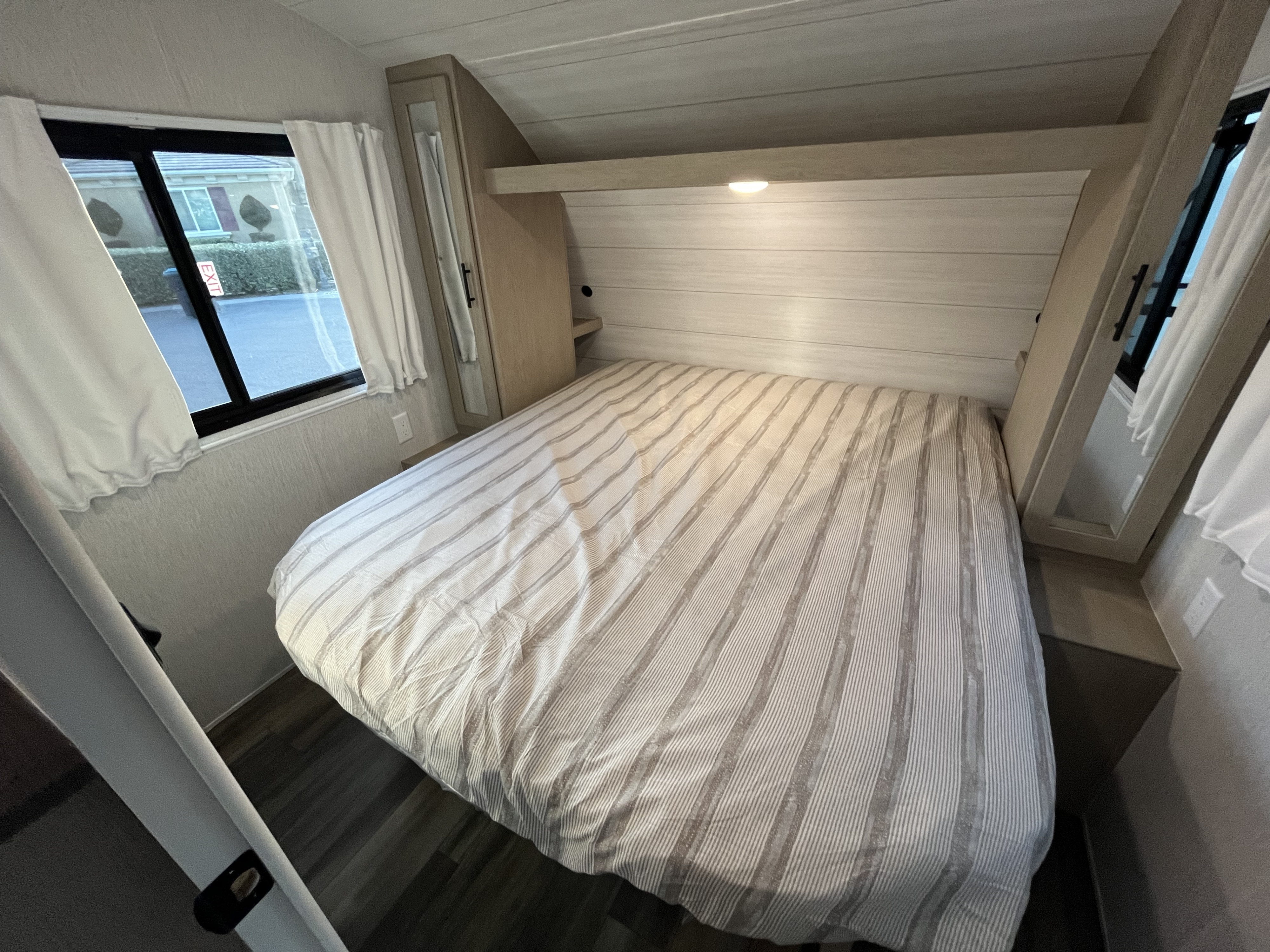 Cozy RV rental bedroom with striped bedding, built-in storage, and a window view of an outside street.. Forest River Evo 2490 2023