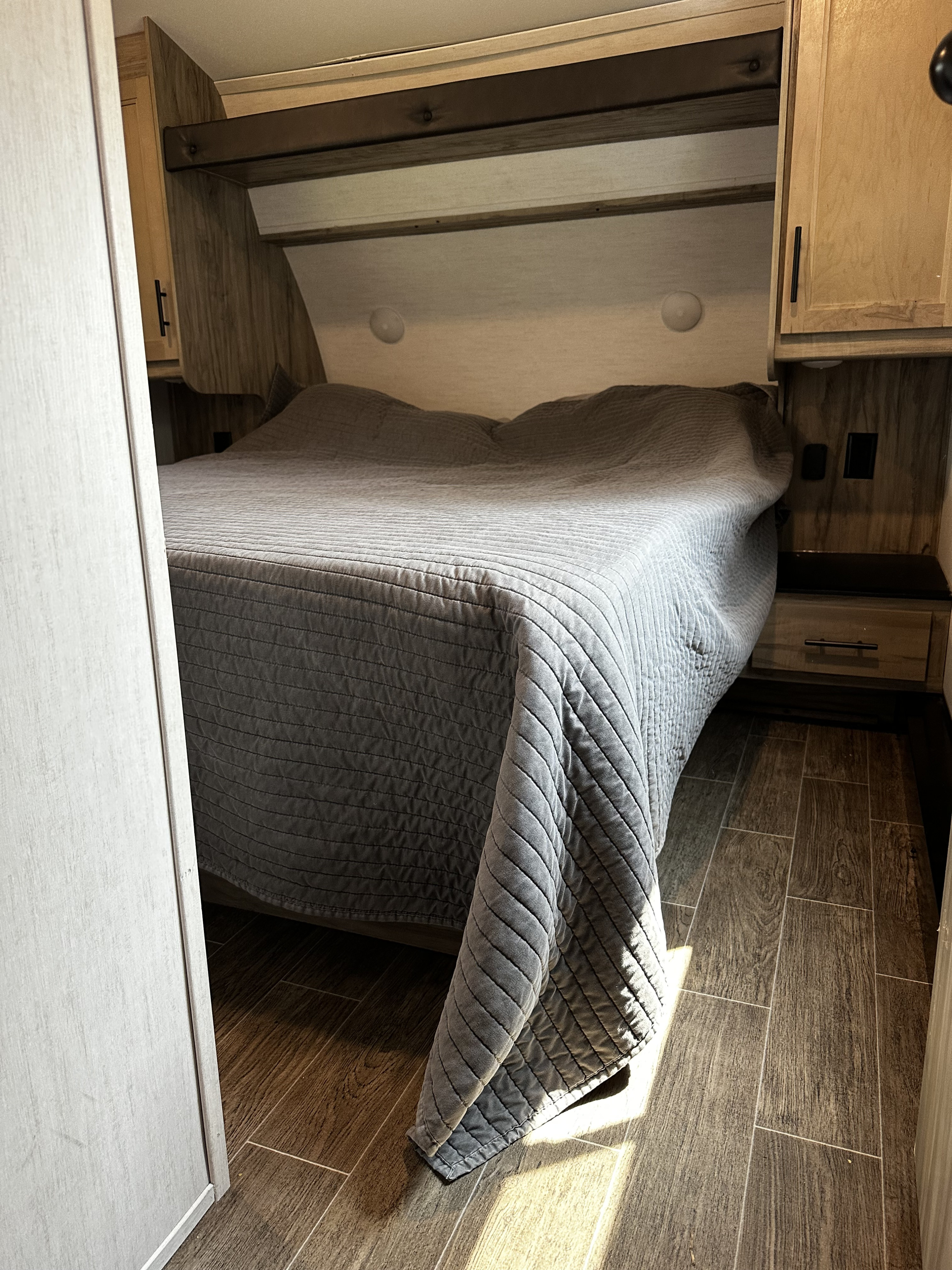 RV rental bedroom: A comfy bed with gray quilt & wood-look floors in a modern RV interior.. Forest River Cherokee Arctic Wolf 2023