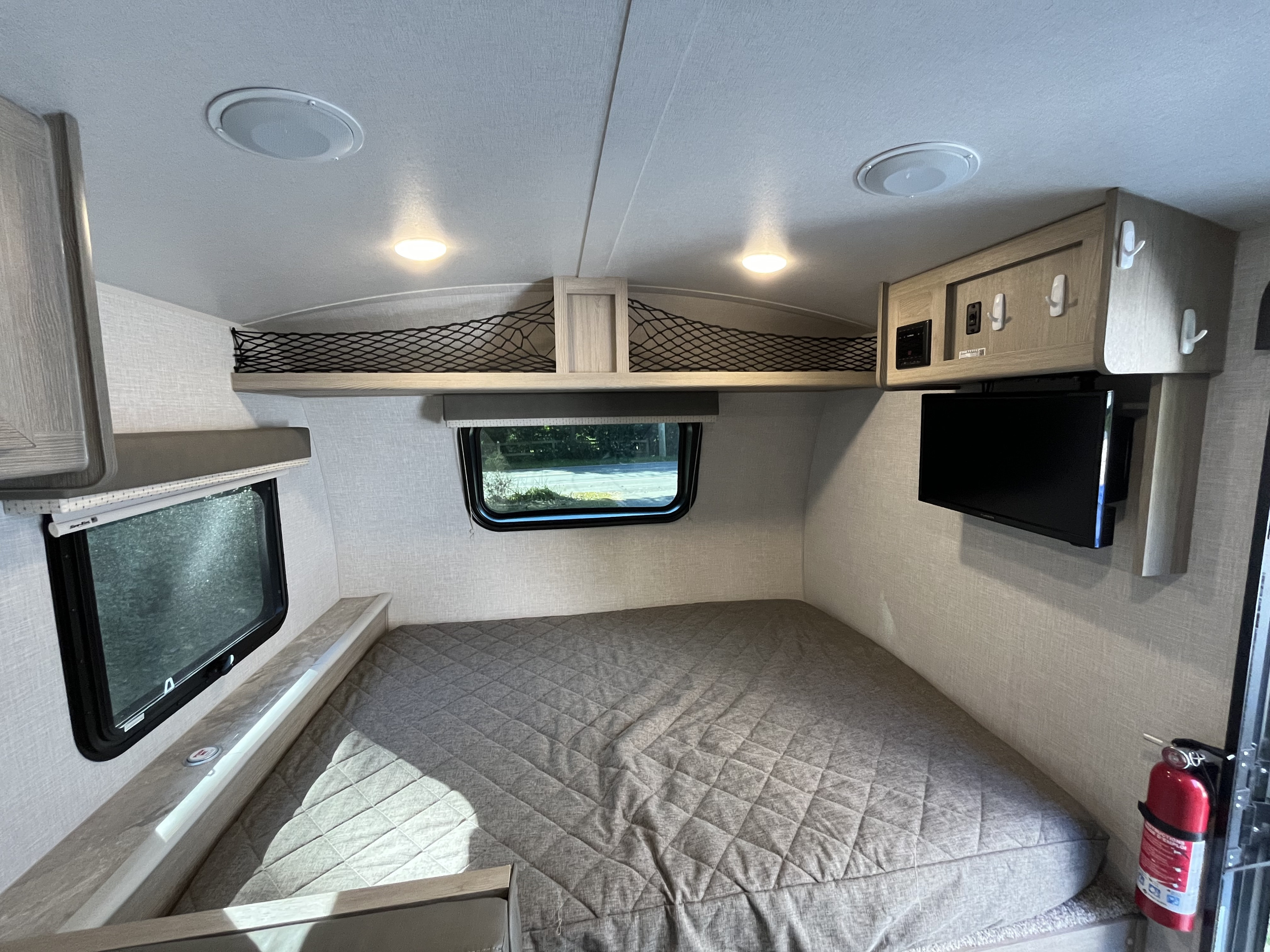 Inside an RV rental: compact bedroom with a quilted bed, window, TV, storage, and fire extinguisher.. Forest River GeoPro 19BH 2021