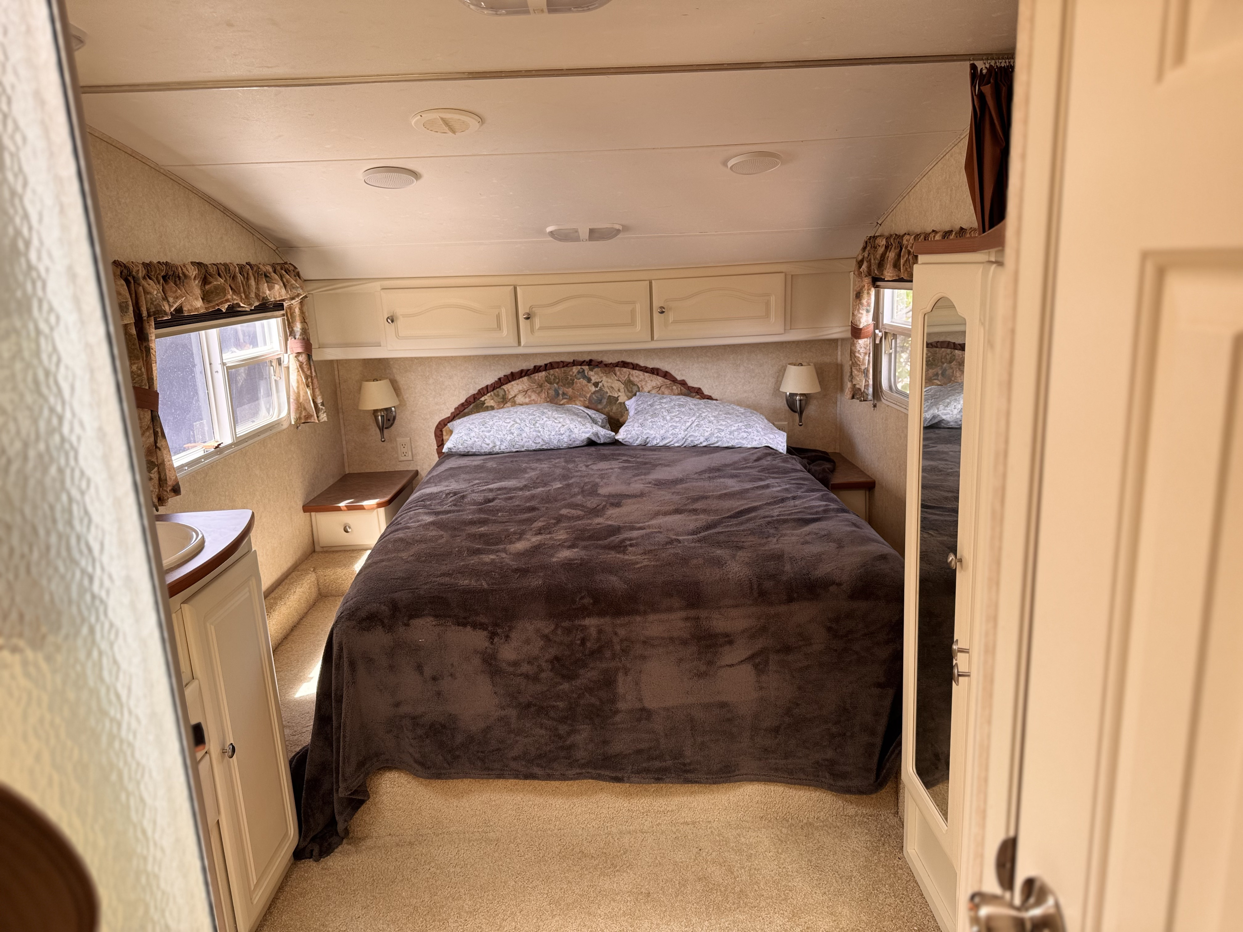 Inside this RV rental bedroom: A large bed, built-in storage, and windows offer a cozy stay.. Keystone RV Outback Sydney 2006