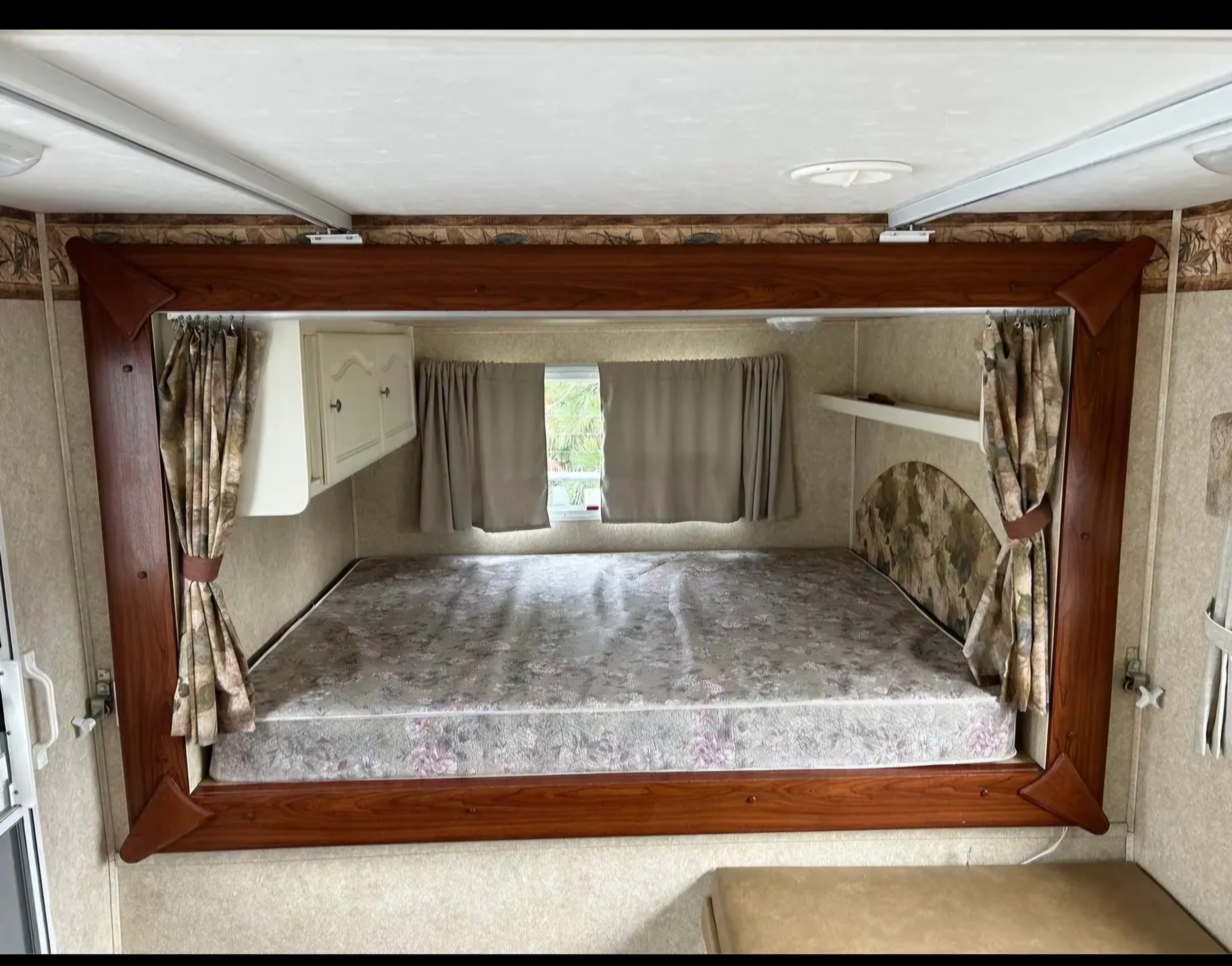 RV rental interior featuring a cozy bed area with a patterned mattress, curtains, and built-in storage.. Keystone RV Outback 2008