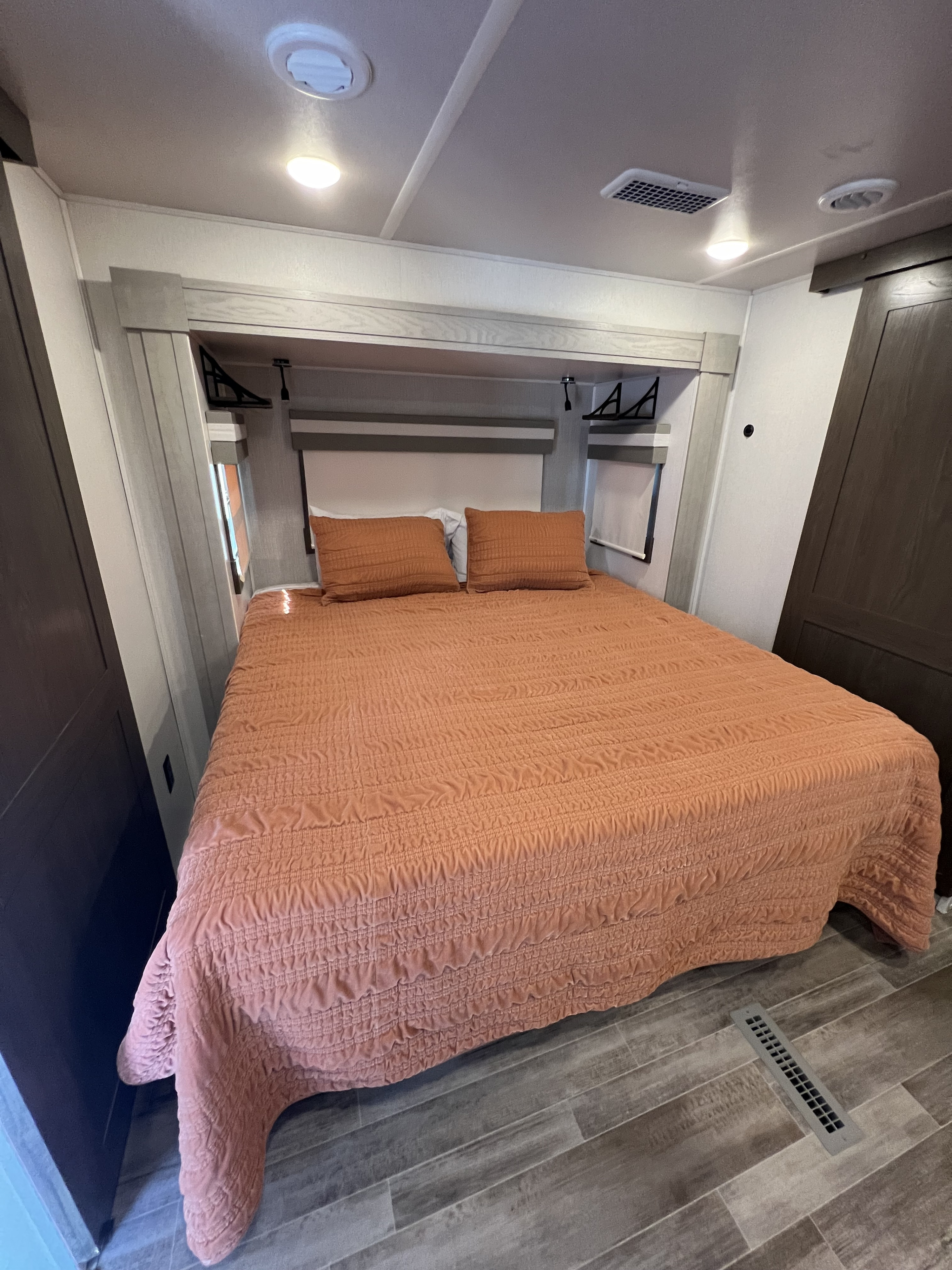 Cozy RV rental bedroom with a large bed, featuring a peach-toned comforter, overhead lights, and built-in storage.. Forest River Palomino Columbus C 2022
