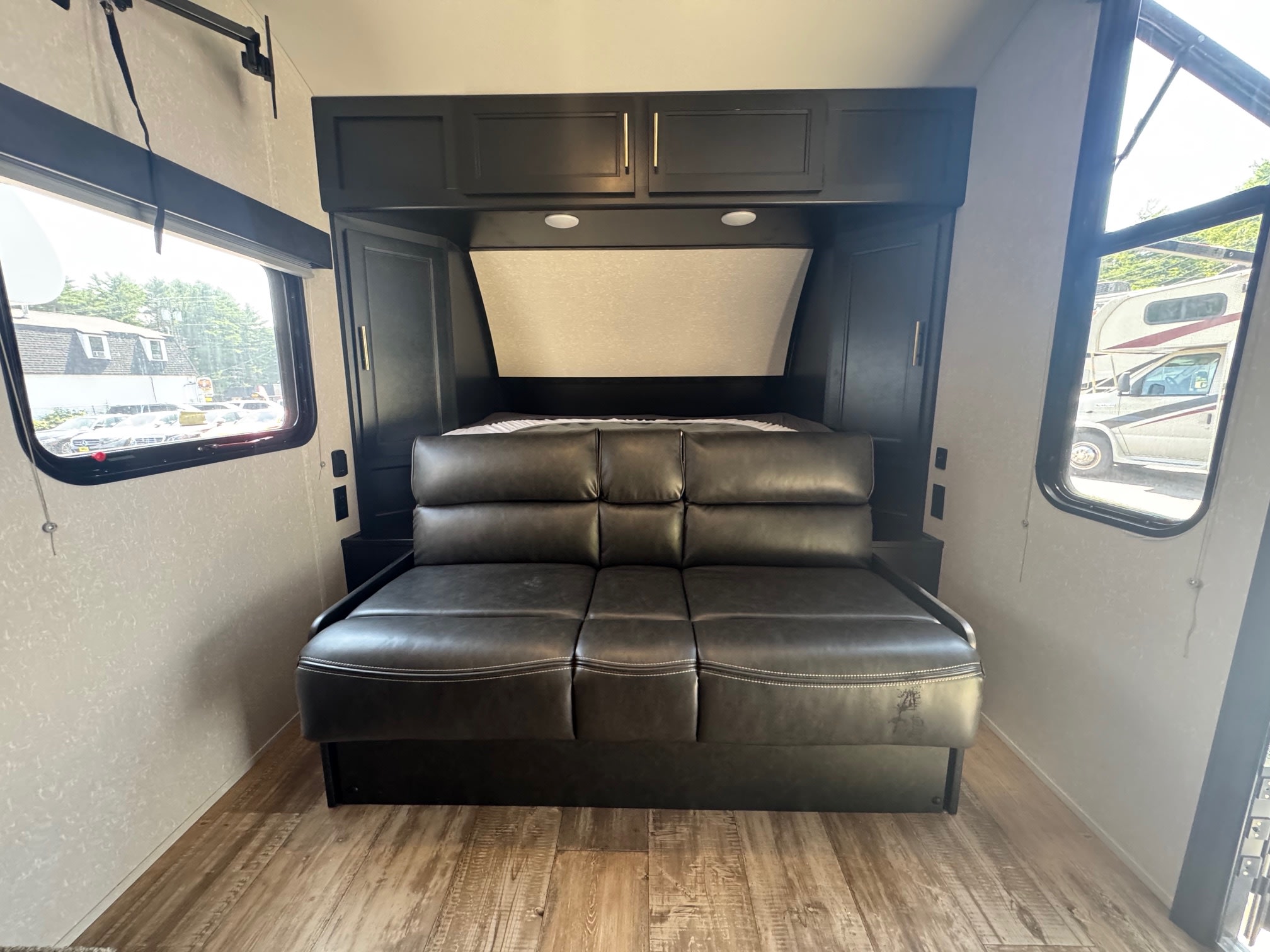 RV rental interior: a sleek black leather sofa that converts into a bed, with overhead storage, lighting, and side windows.. Forest River Cherokee Wolf Pup 2021