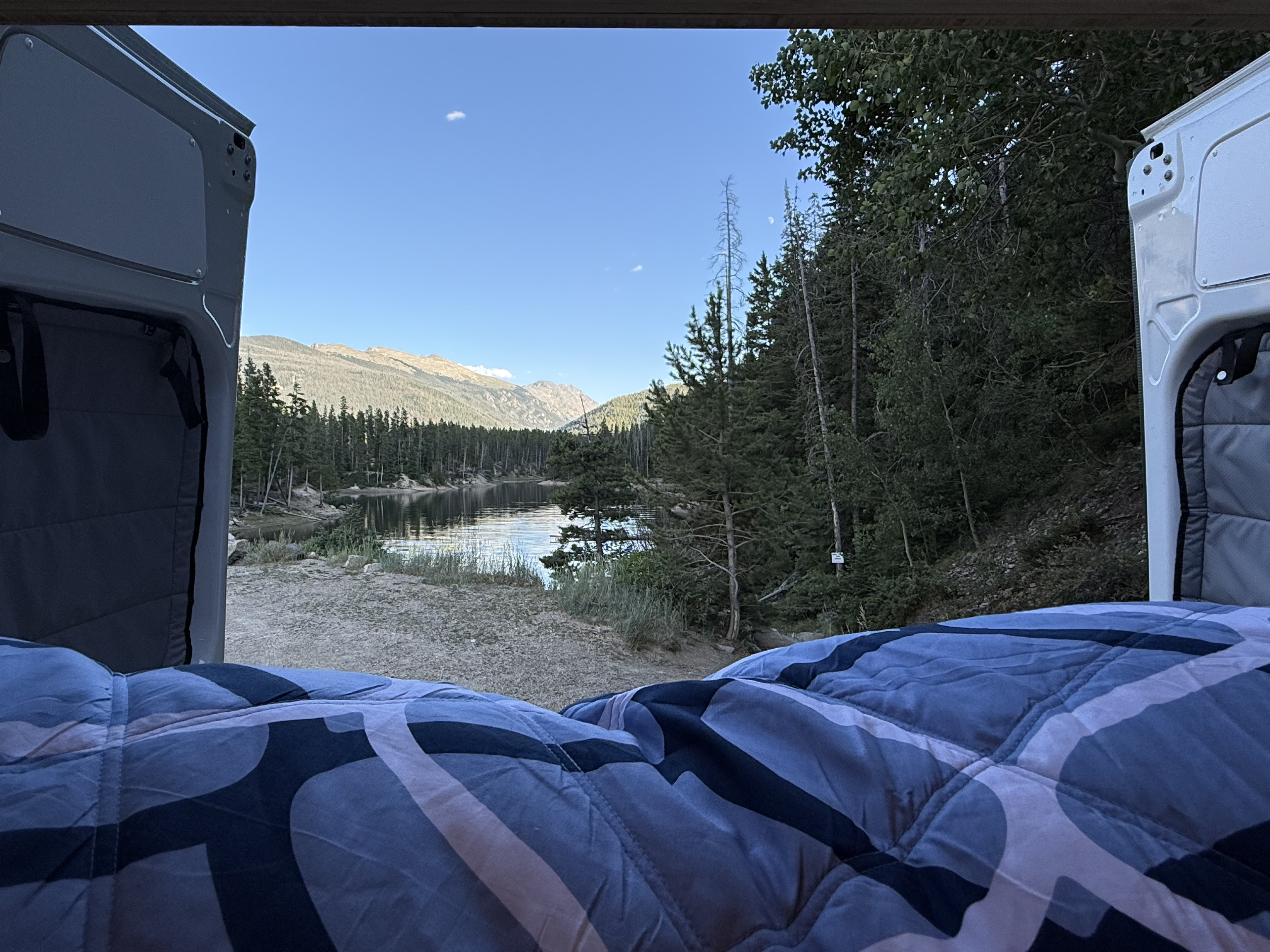 Cozy RV rental bed with serene lake & mountain view. Perfect for peaceful van life camping adventures.. Mercedes-Benz Sprinter 2024